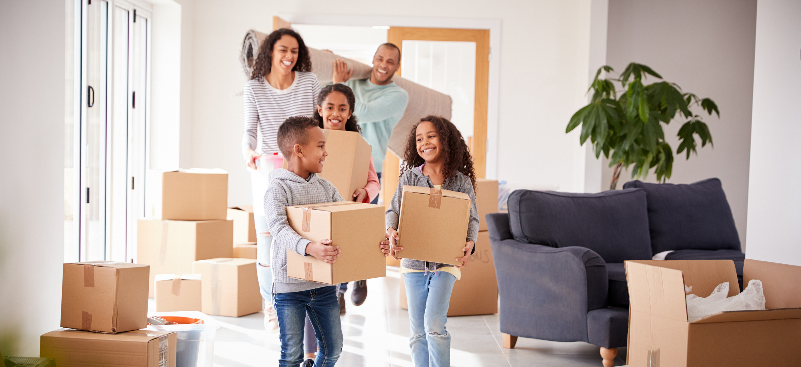 A family of five smiles while moving boxes into a house.