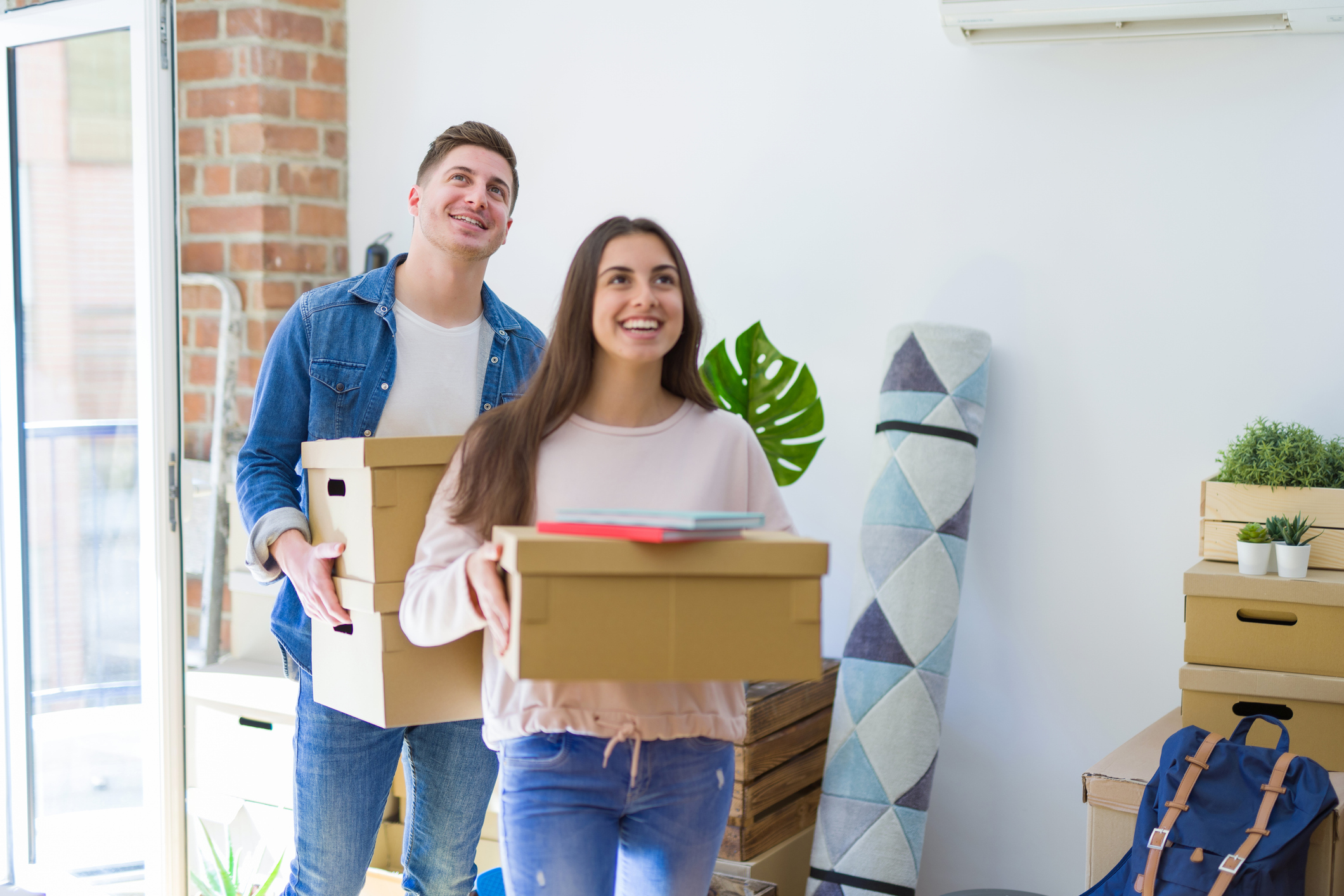 A man and a woman smile while moving boxes into a house.