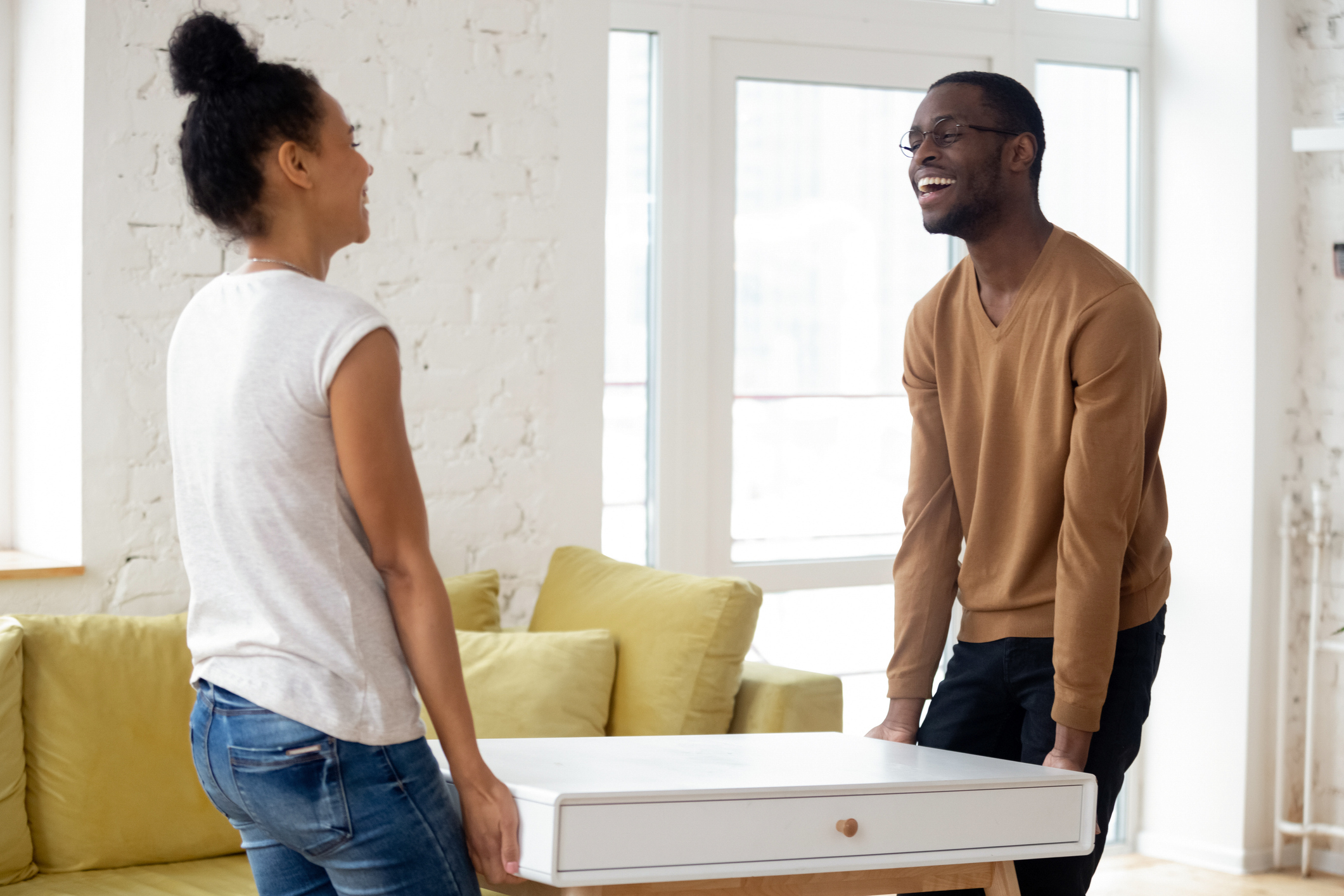 A man and a woman smile while moving a box into a house.