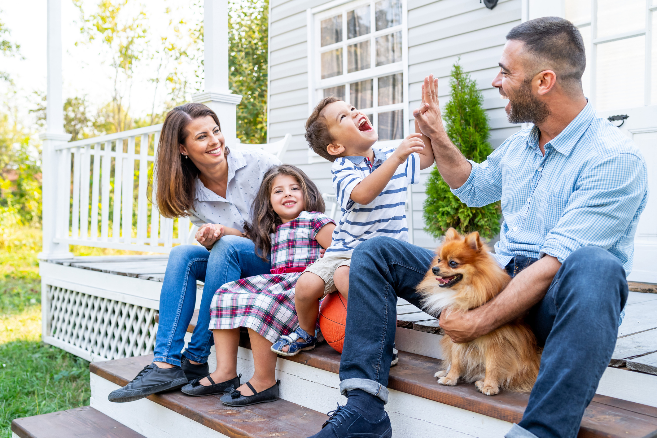 A family of four sits on their front porch steps with their pomeranian. 
