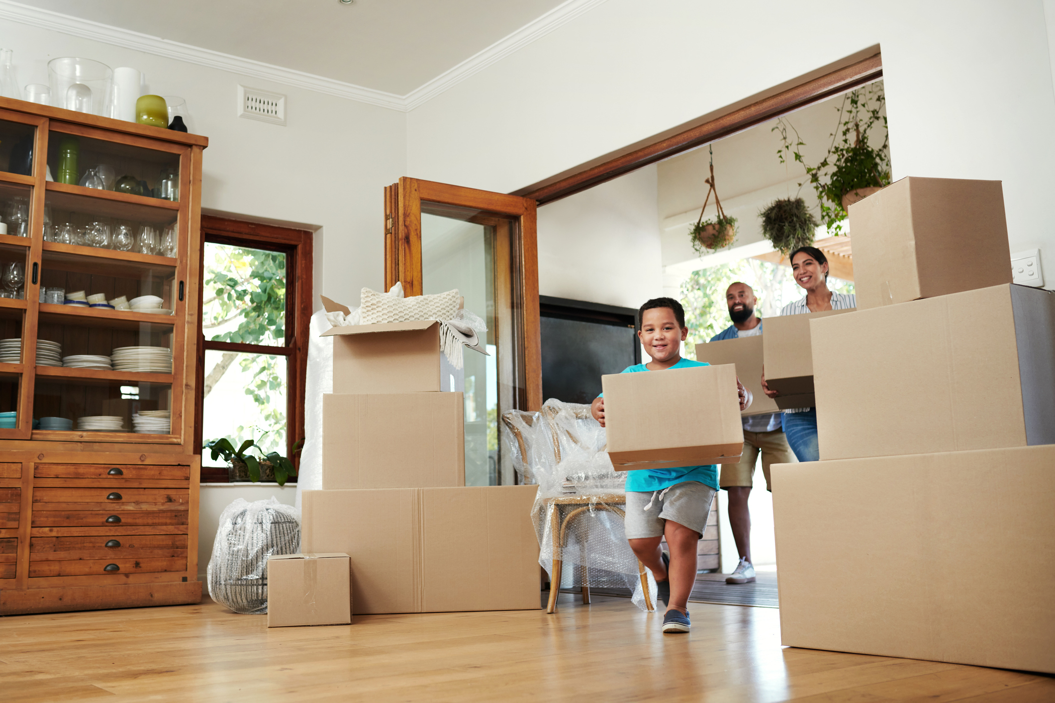 A family smiles while moving boxes into a new house.