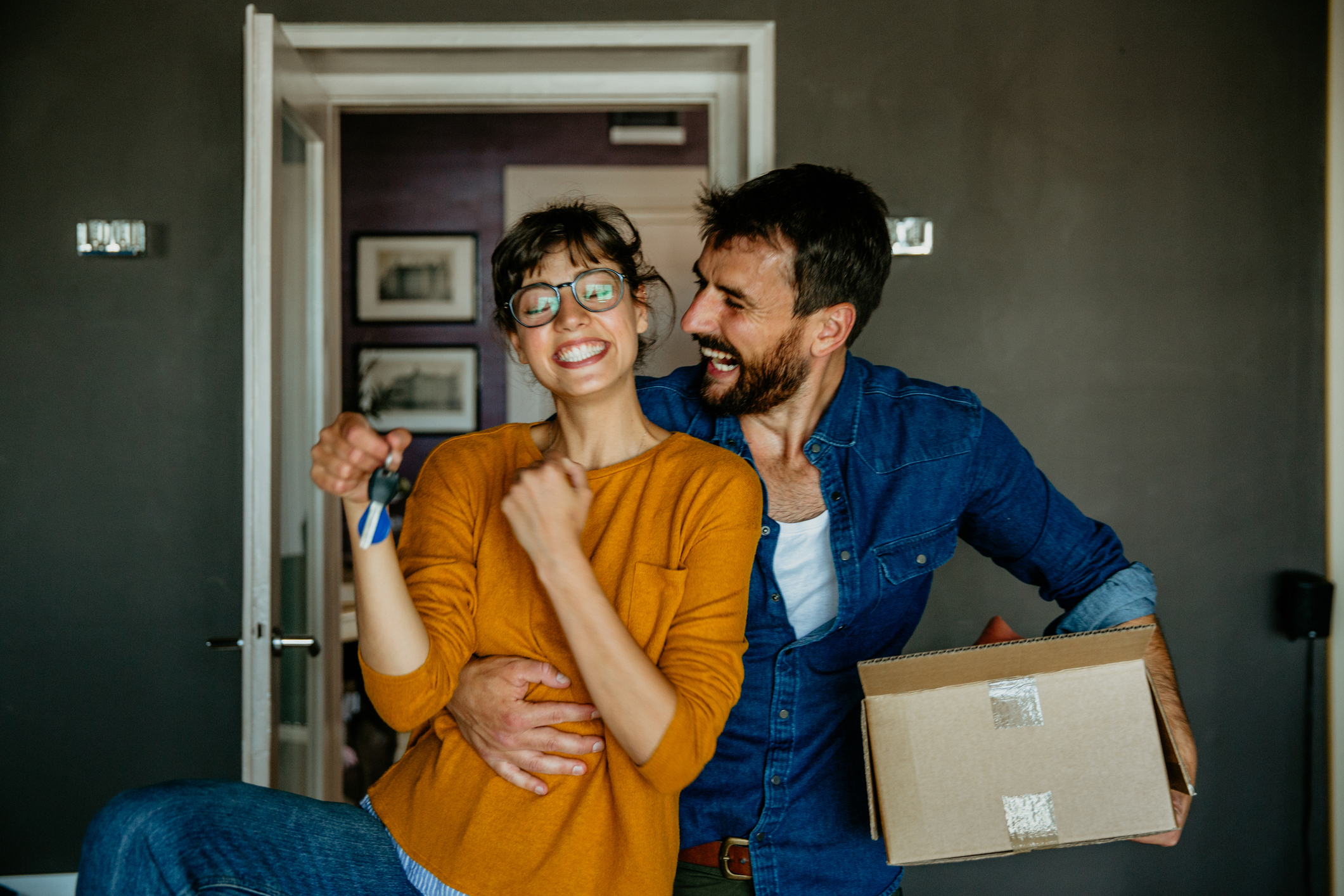 A man and a woman smile while holding keys and boxes.
