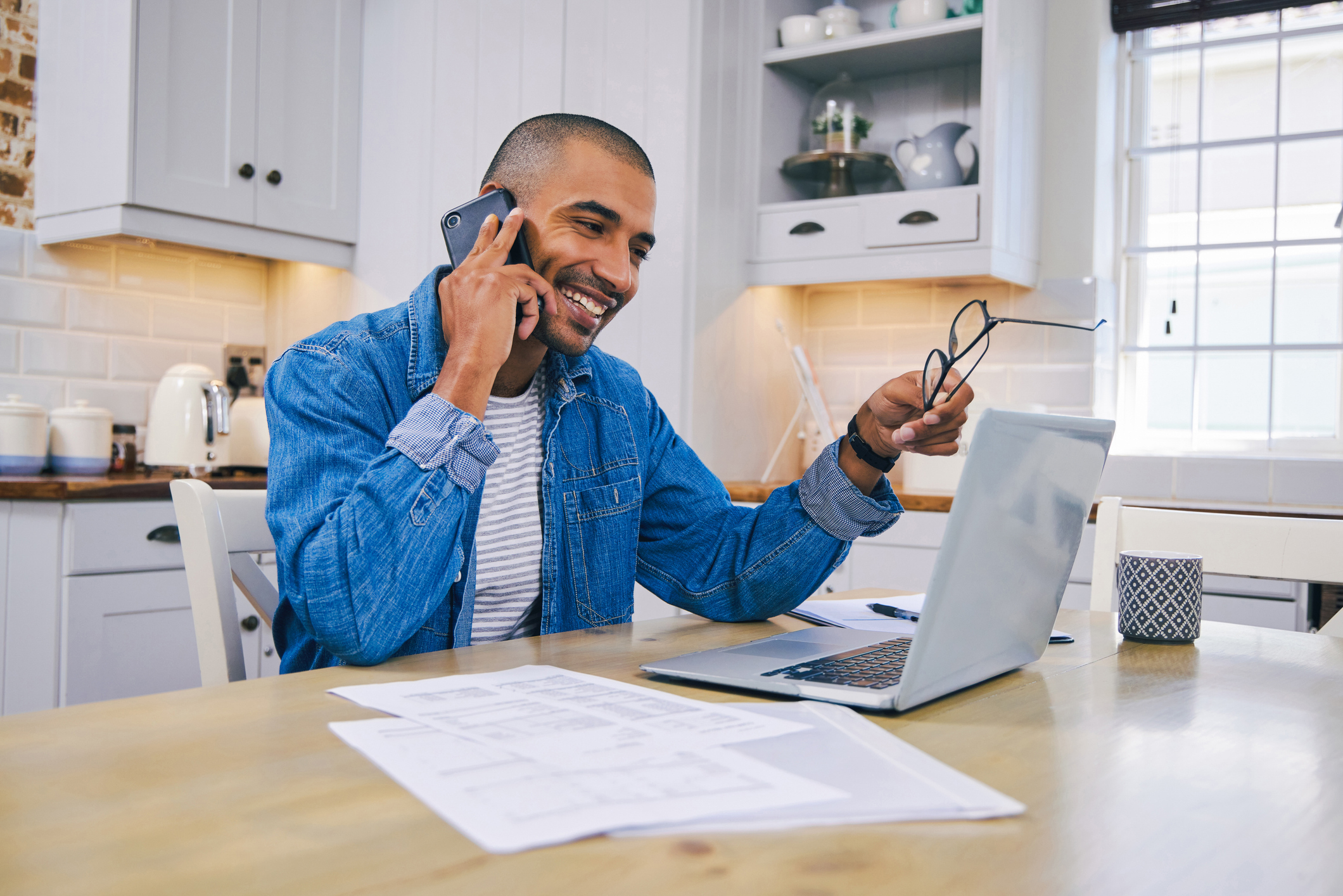 A man smiling while talking on a cell phone and working at a laptop. 