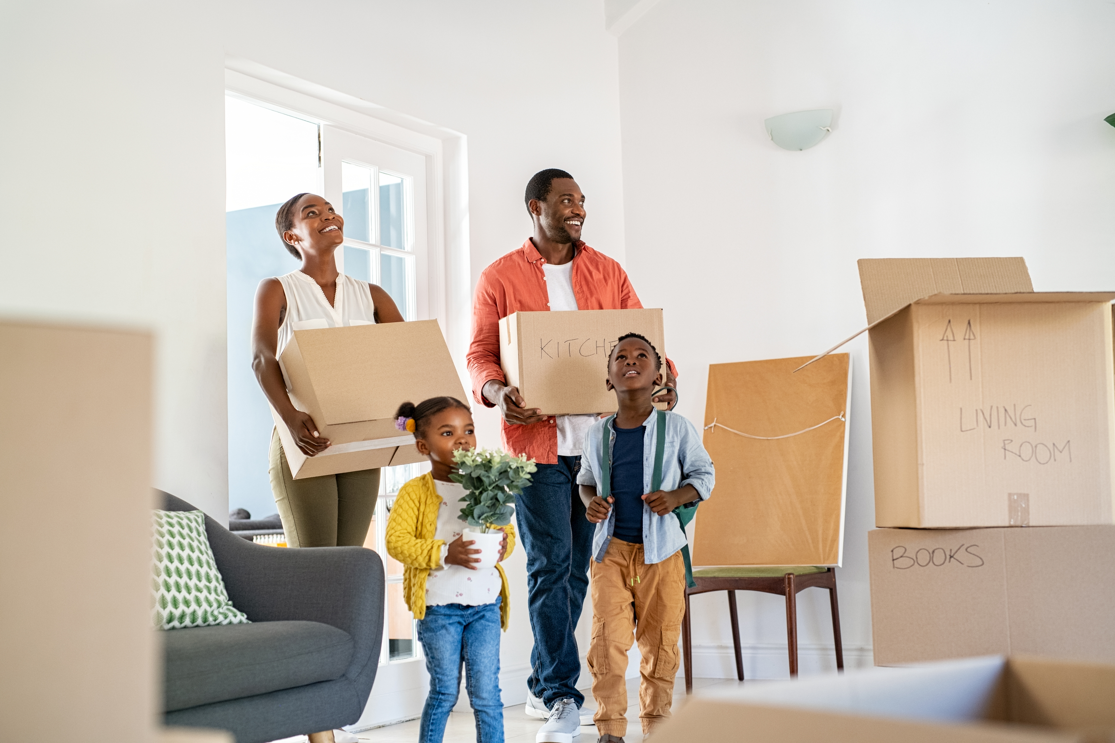 A family of four smiles while moving boxes into a new home.