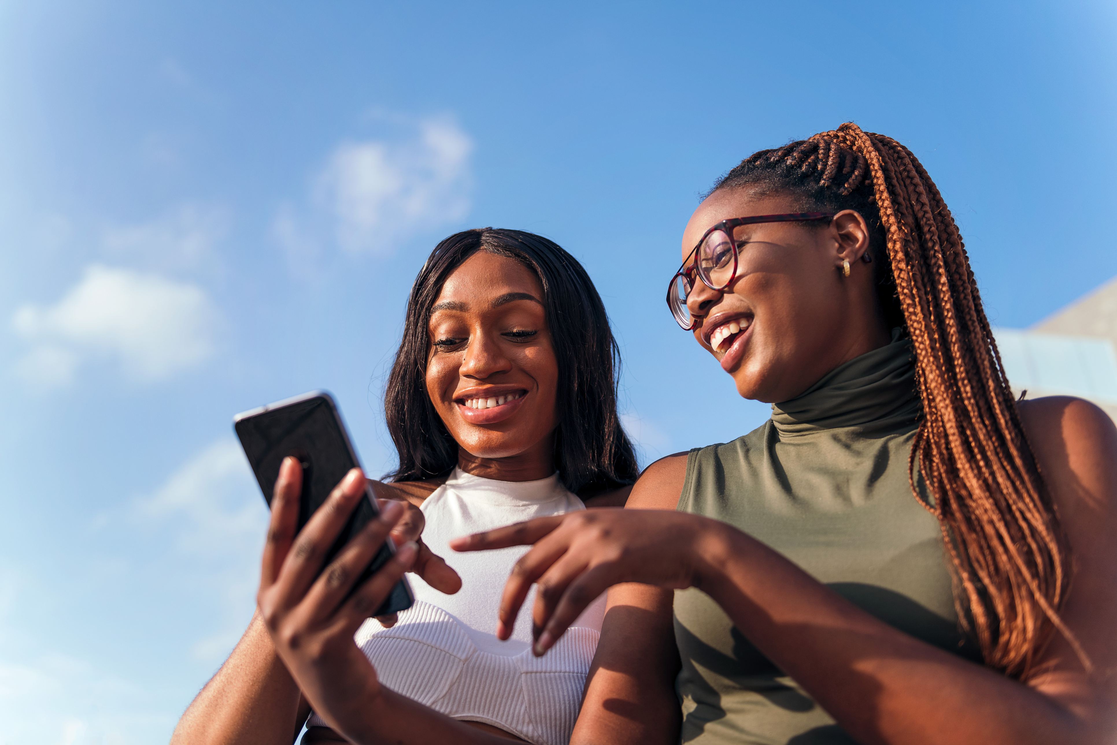 Two women smile at a phone.