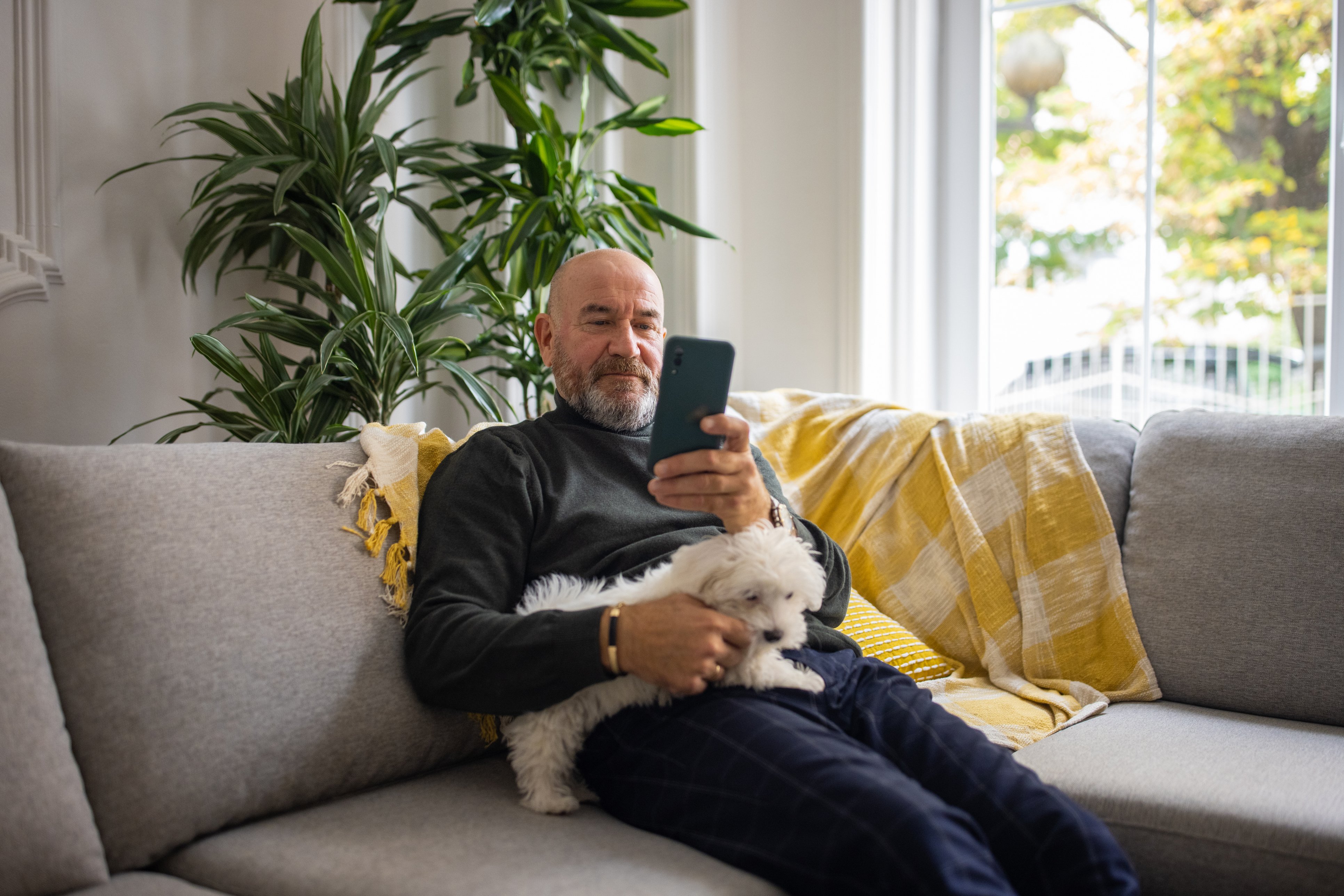 A man smiles at a phone while holding a little white dog.