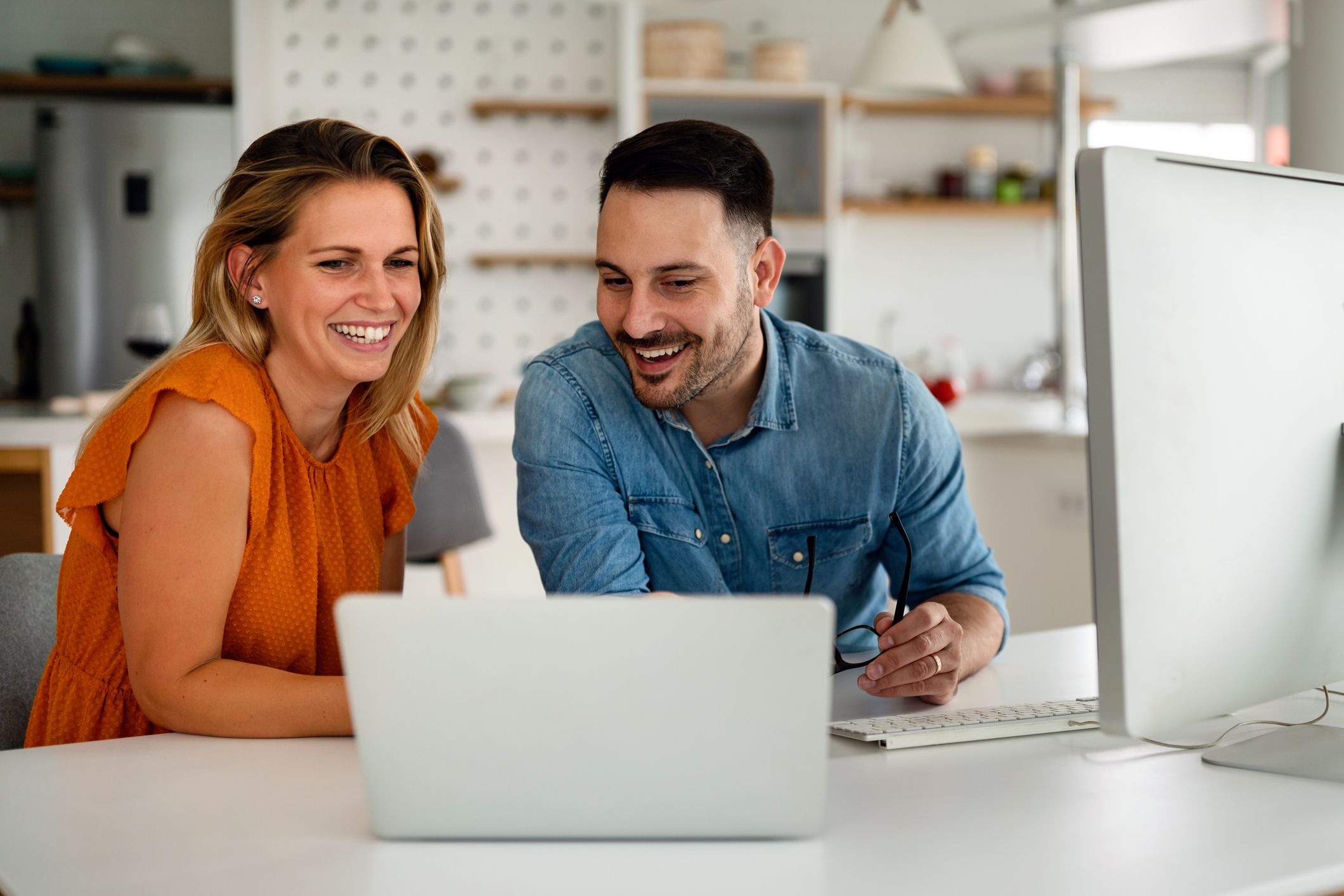 A woman and a man smile at a laptop.