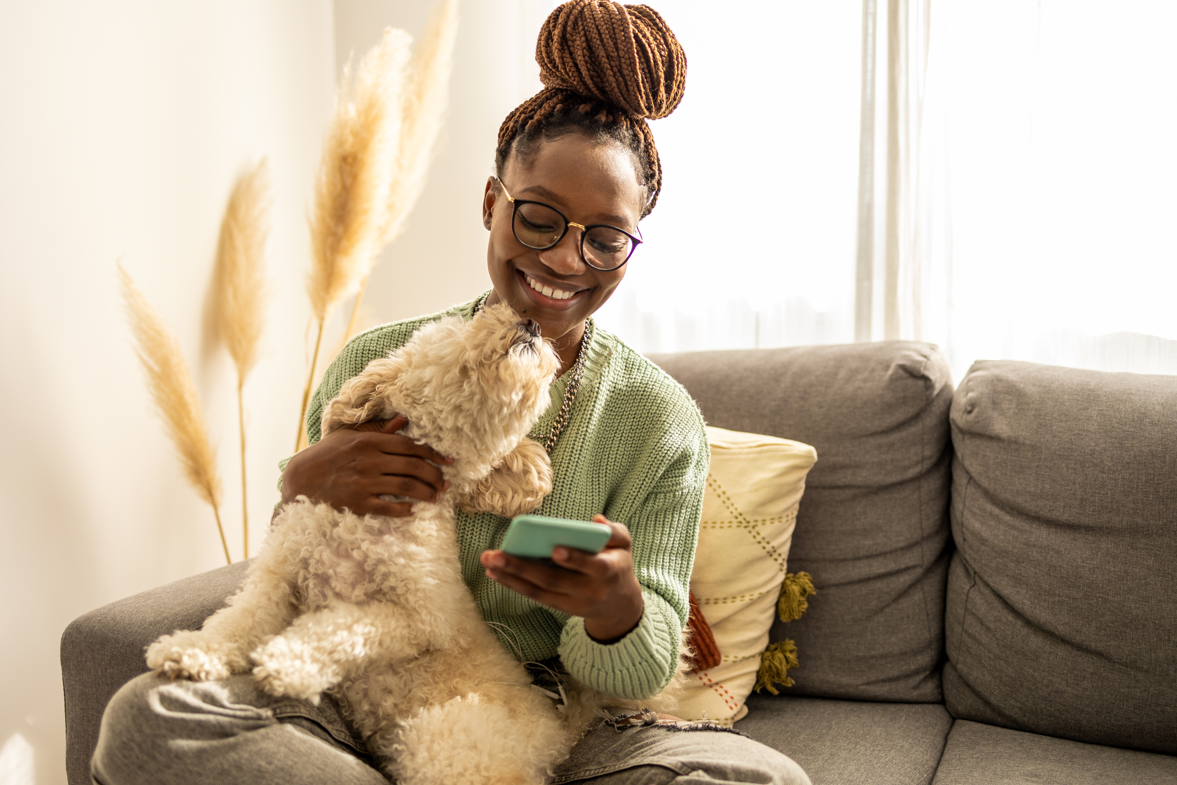 A woman smiling at a phone while holding a Bichon Frise.