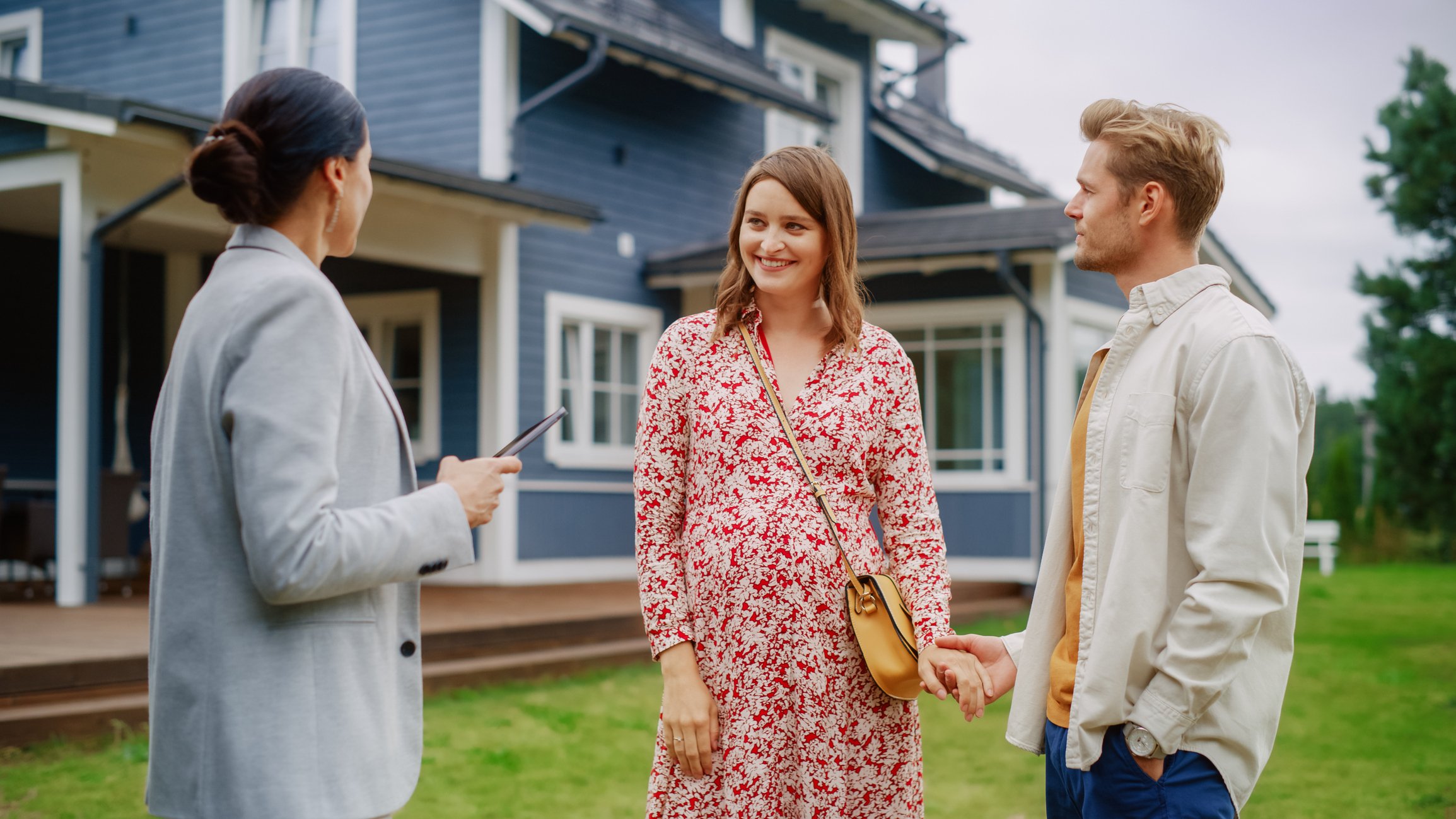 A man and woman smile while a real estate agent shows them a house.