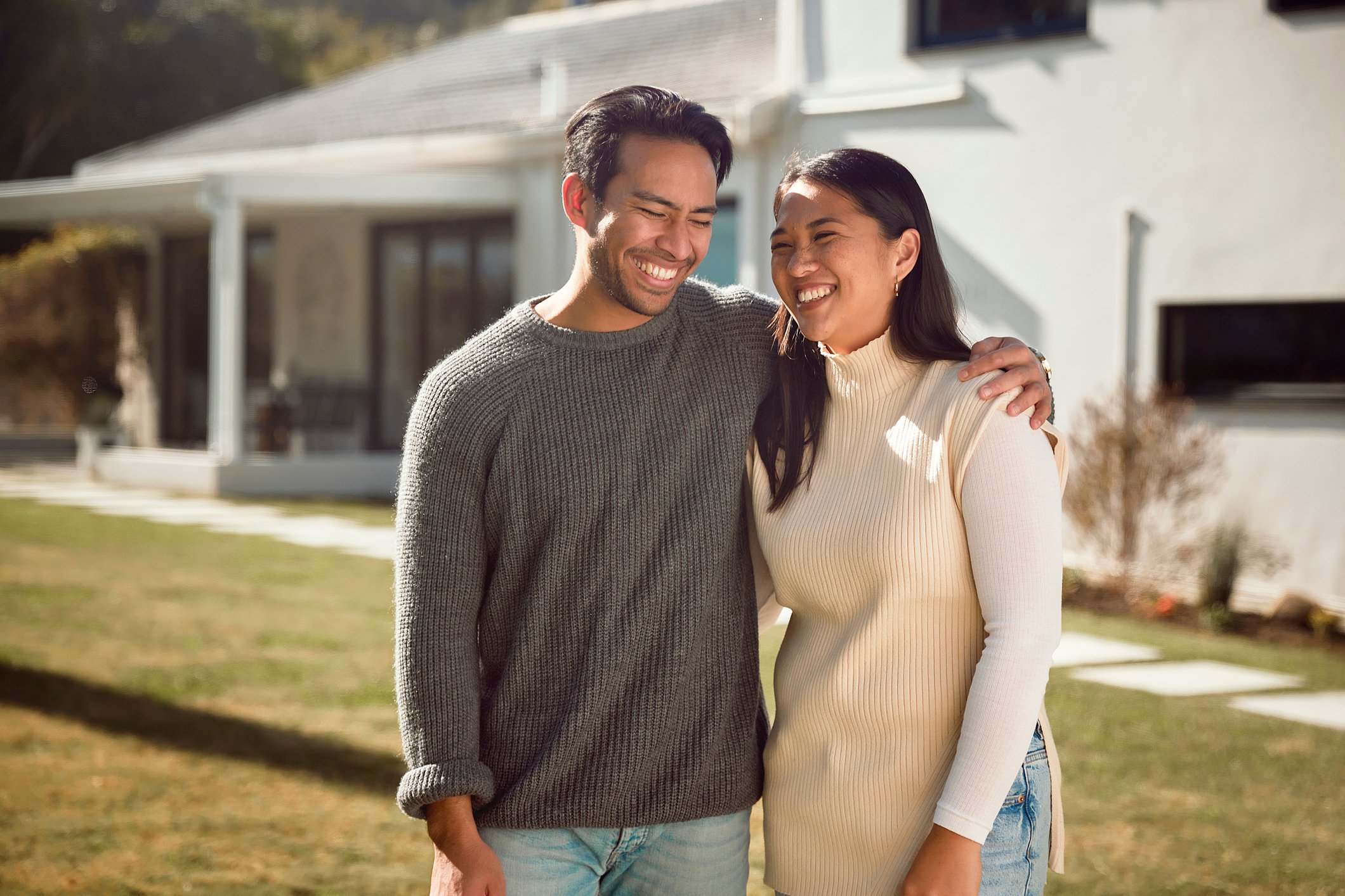 A man and a woman smiling in front of a house.