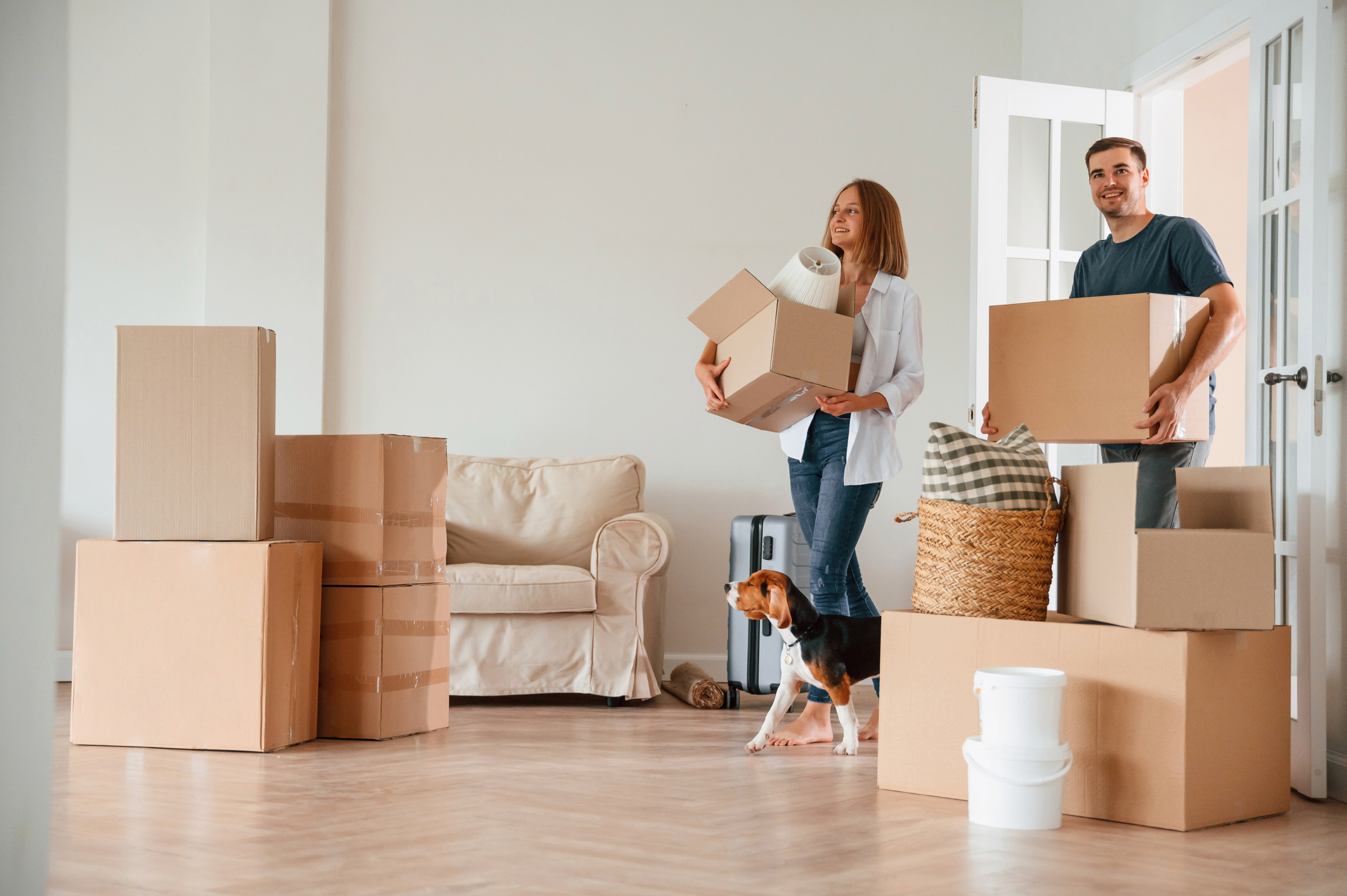 A man and a woman smile while carrying boxes into a new house.