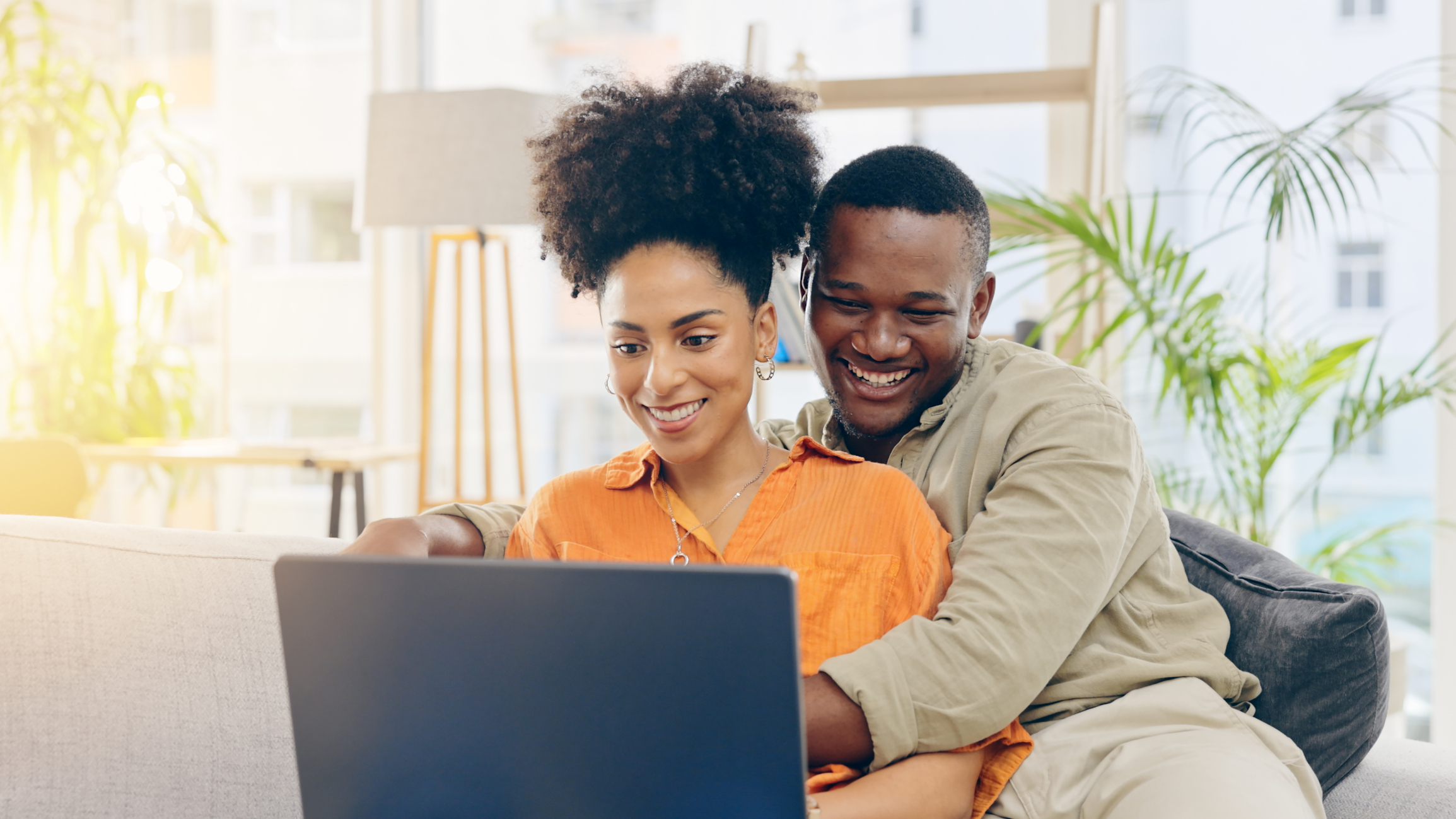 A man hugging a woman while they both smile at a laptop.