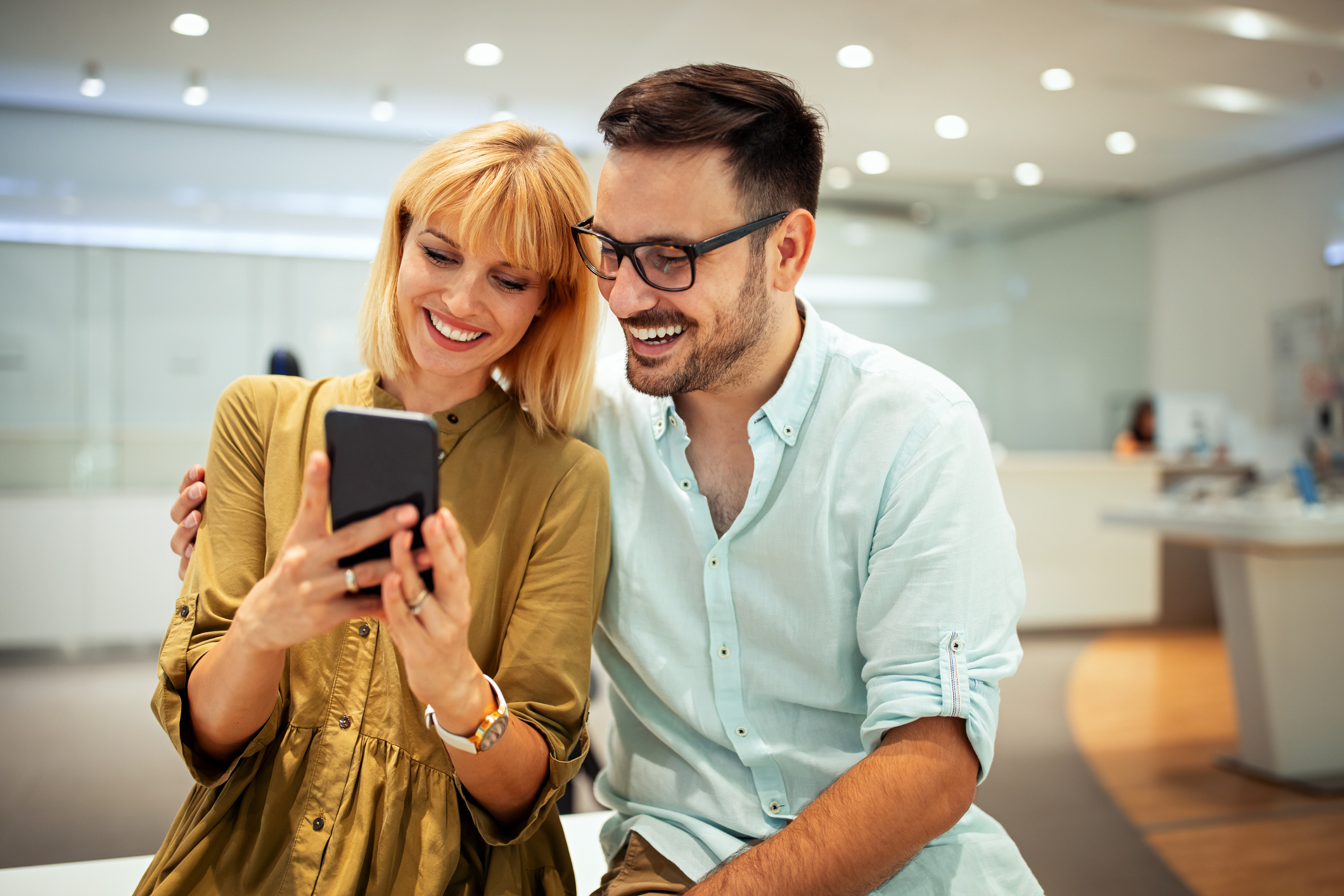 A man and a woman smile while looking at a phone.