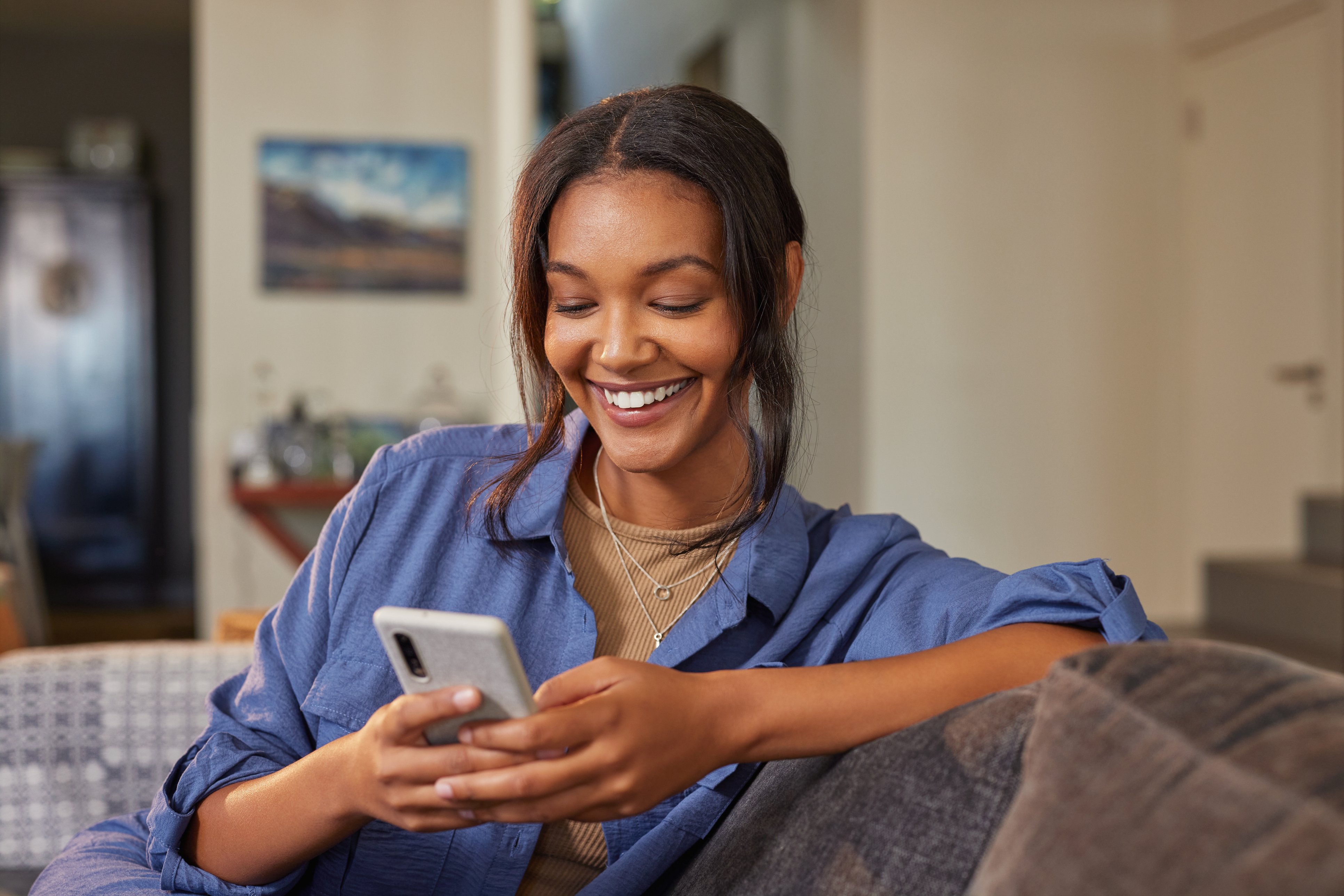 A woman smiles at a phone while estimating her refinance closing costs.