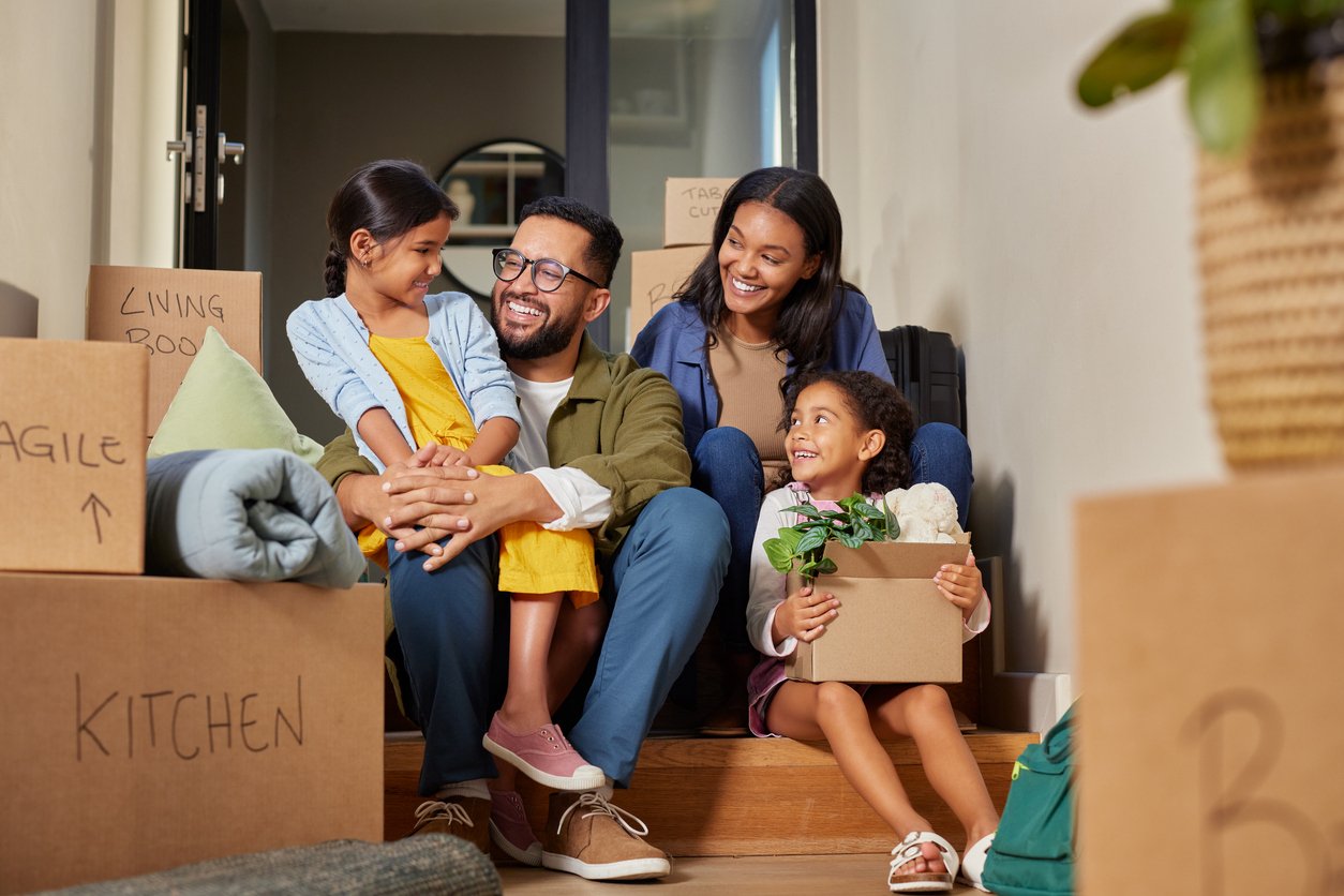 A family smiles while surrounded by moving boxes. 