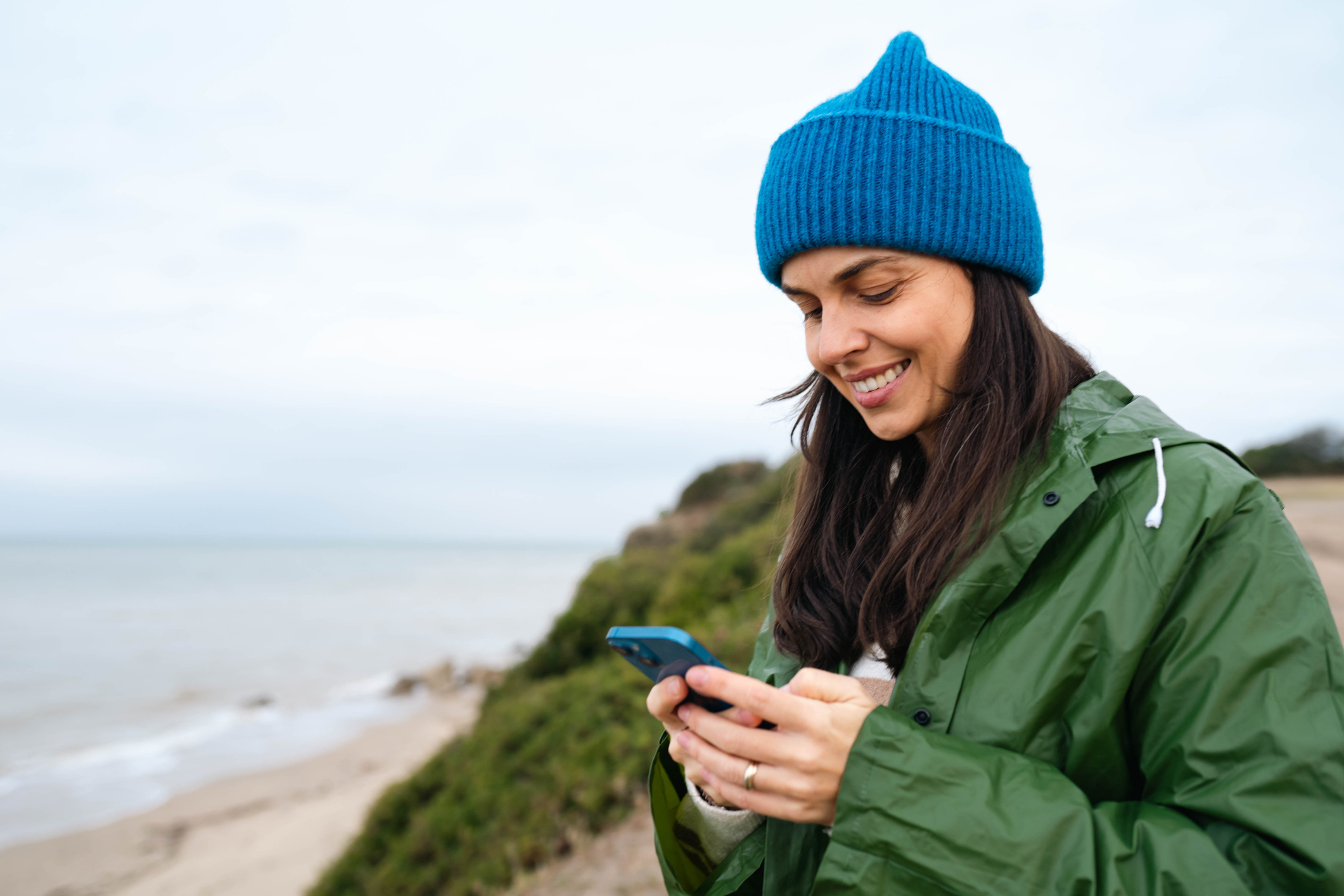 A woman smiles at a phone on a hilly west-coast beach.
