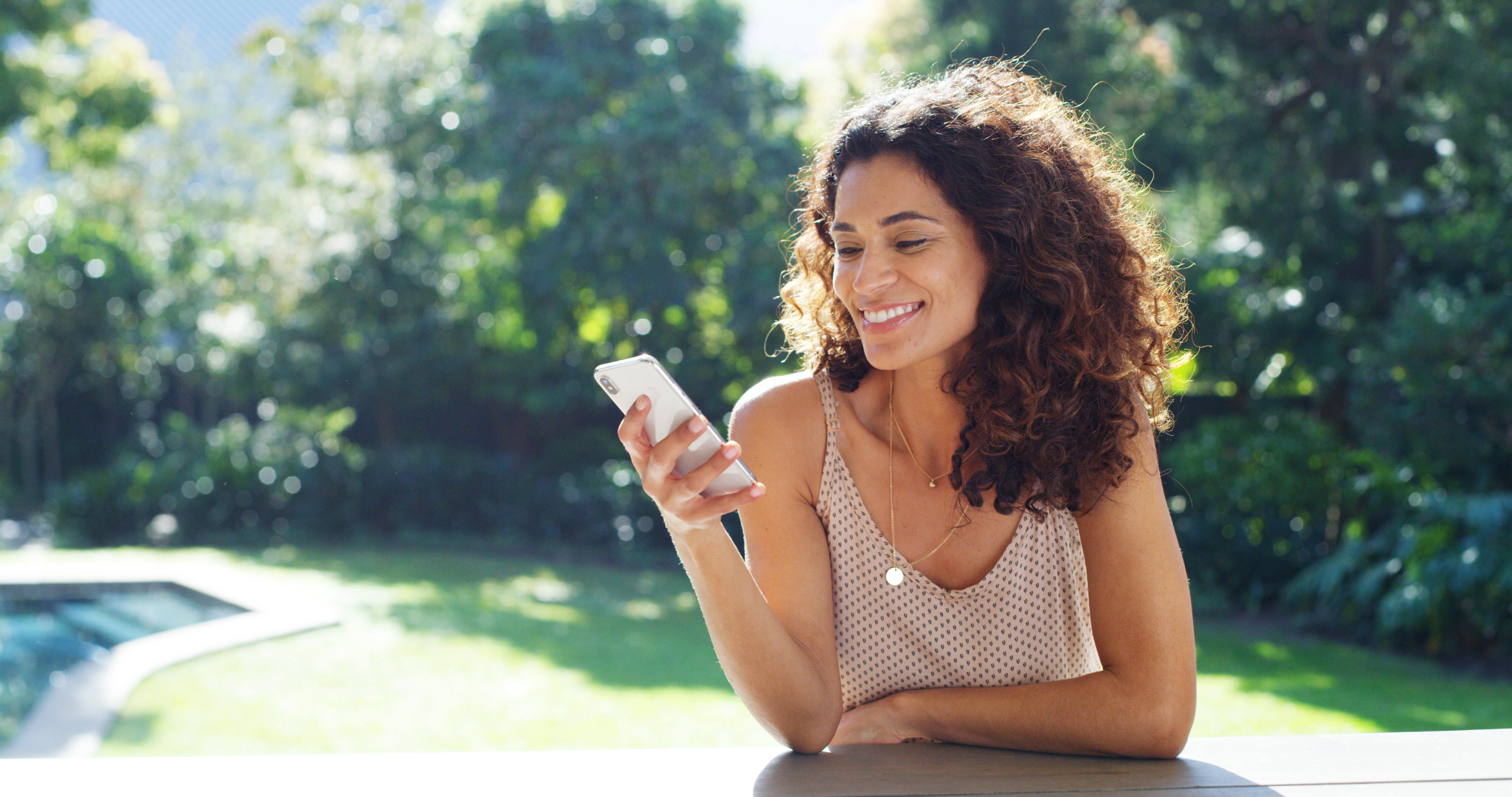 A woman smiles while comparing FHA and conventional mortgage options on her phone.