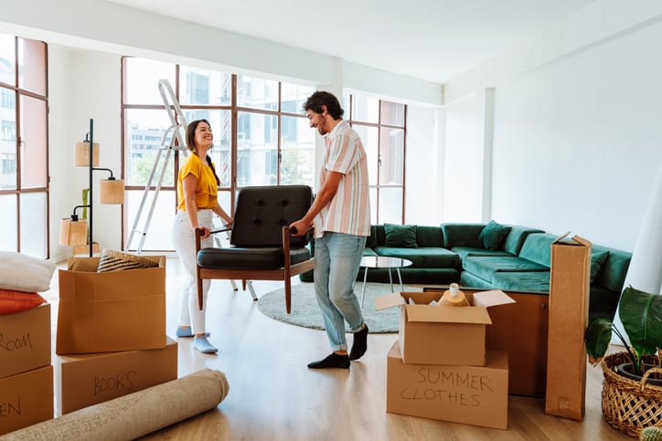 A man and a woman carry a chair into a house.