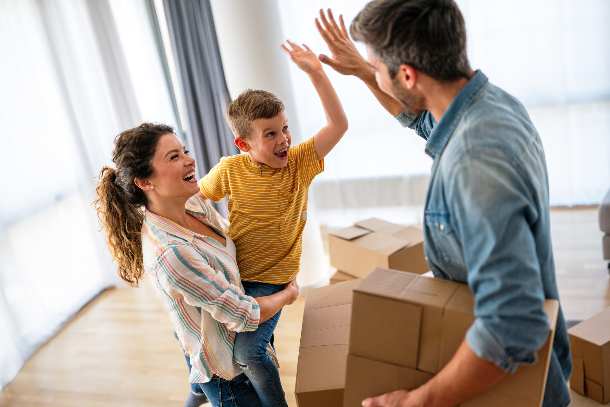 A man, woman, and child high-five while moving boxes into a house. 