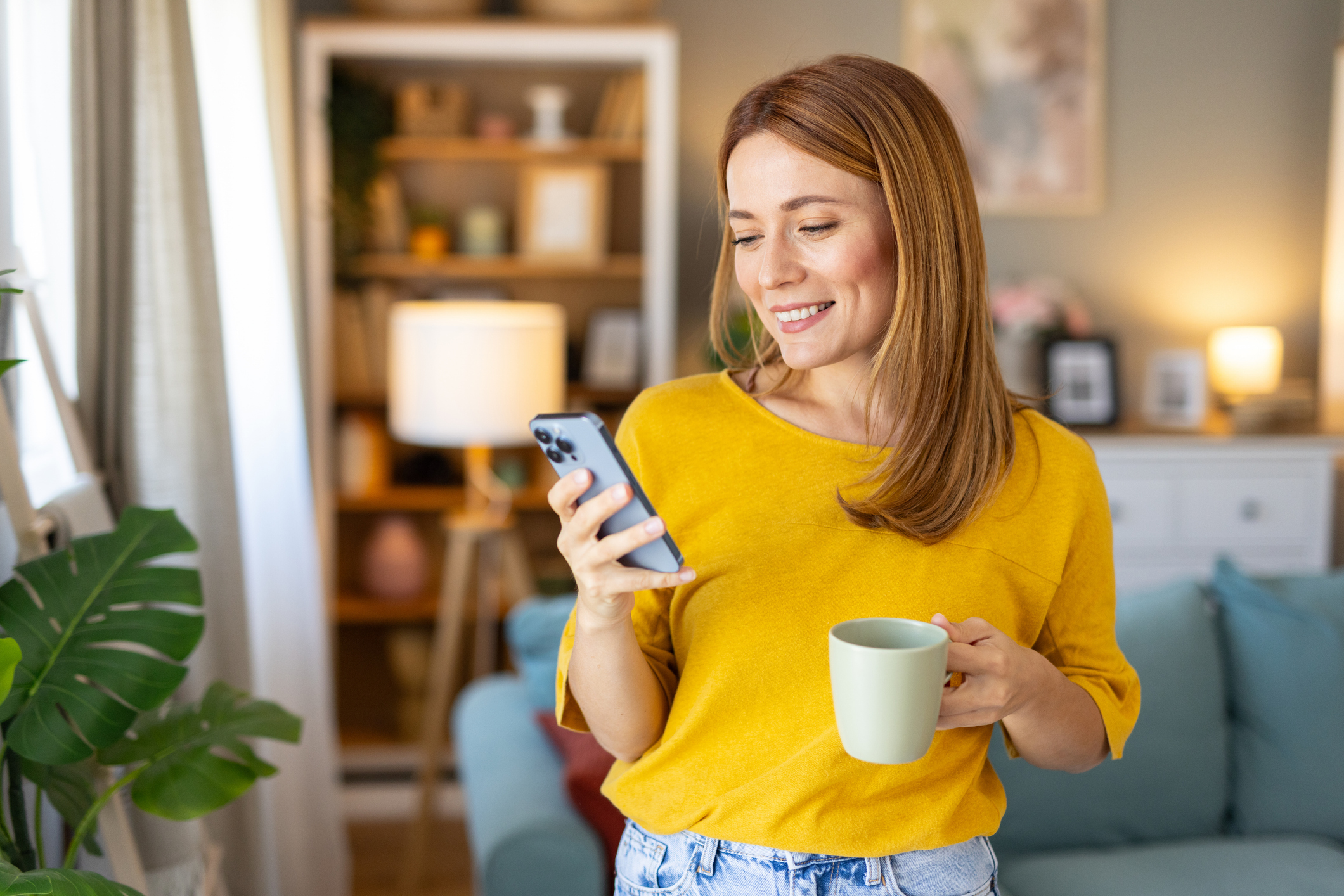 A woman smiling at a phone and holding coffee.