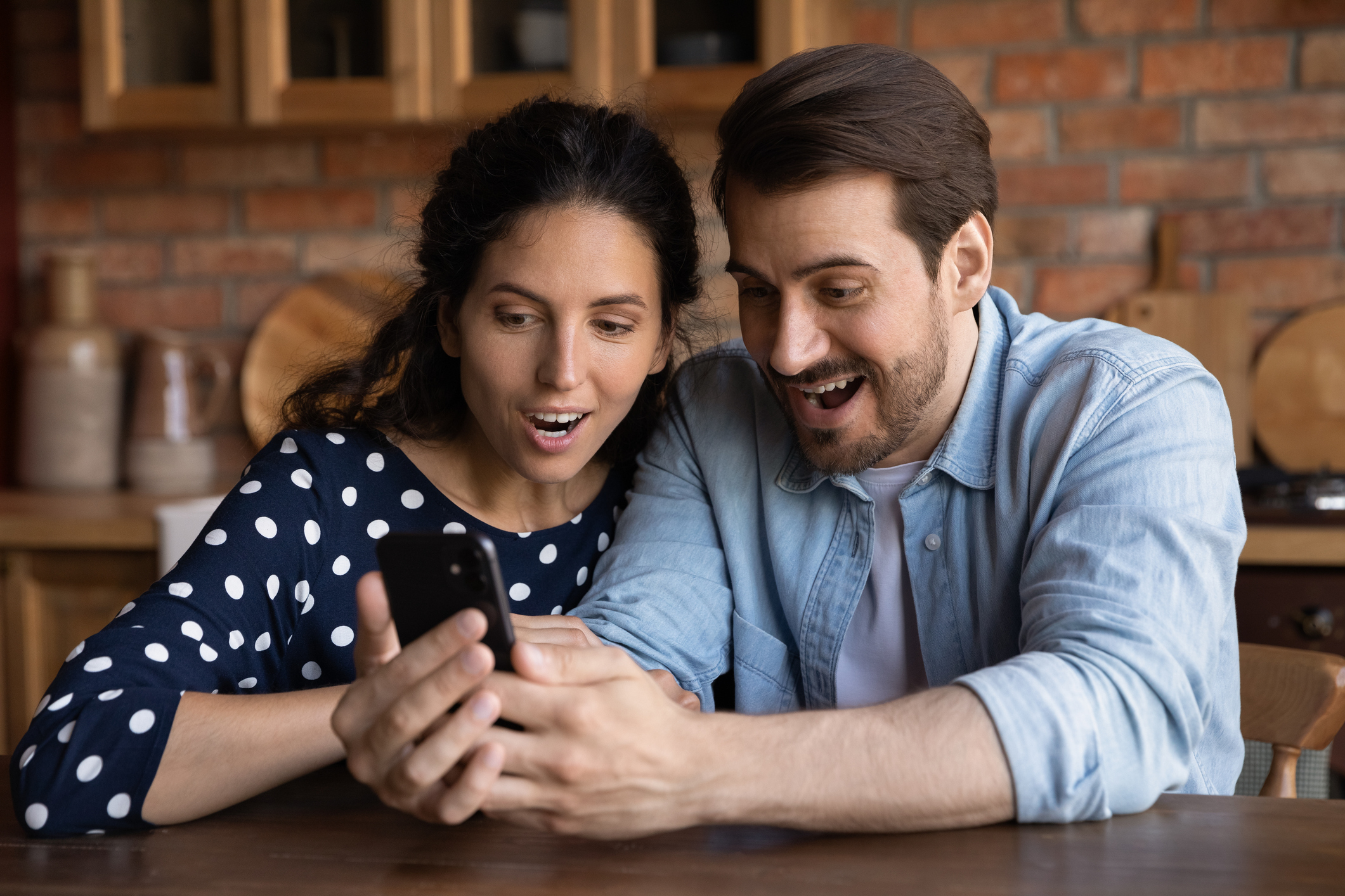 A man and a woman smiling with surprise while looking at a cell phone.