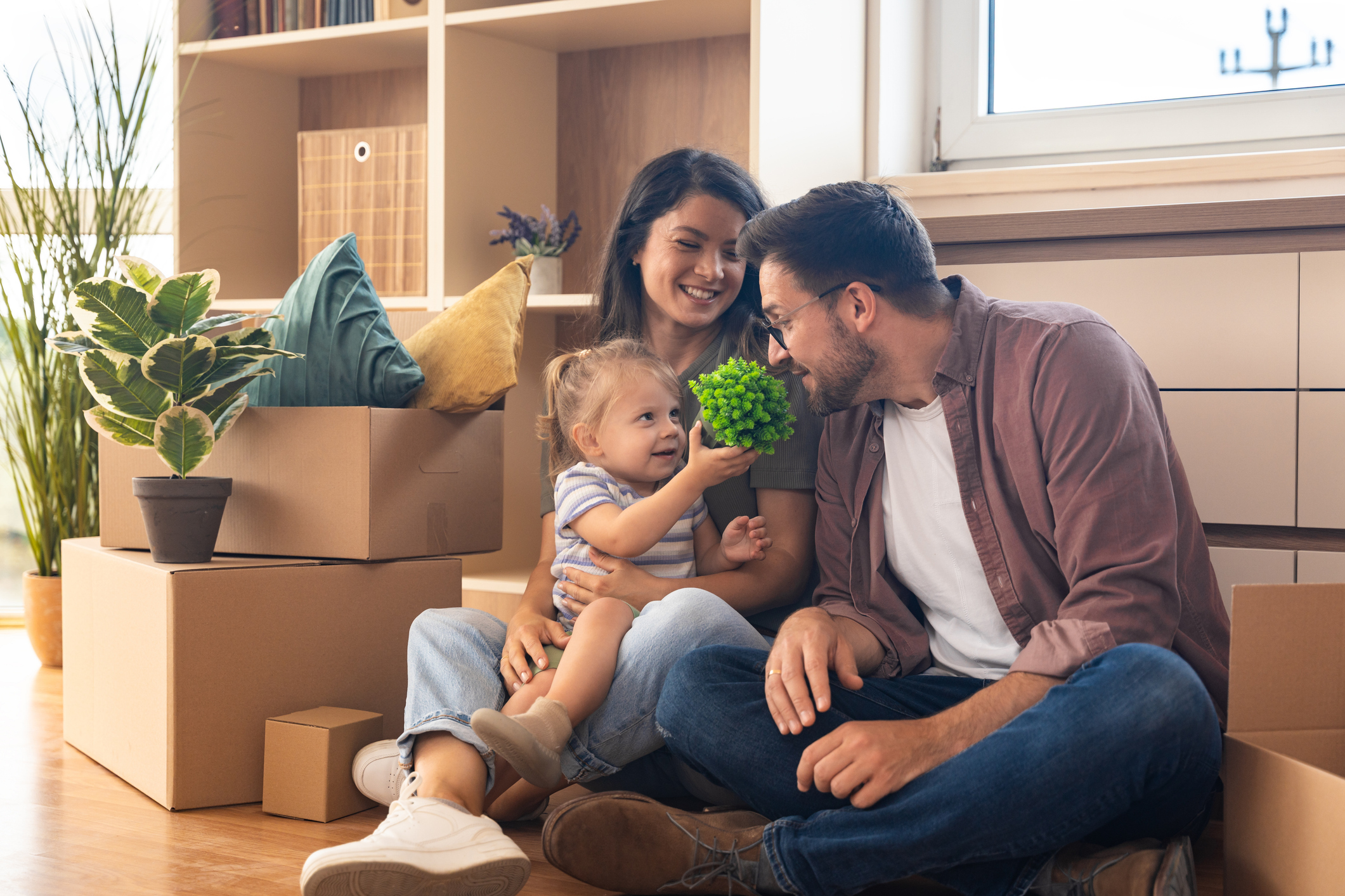 A man, woman, and child sit on the floor of a new home with moving boxes.