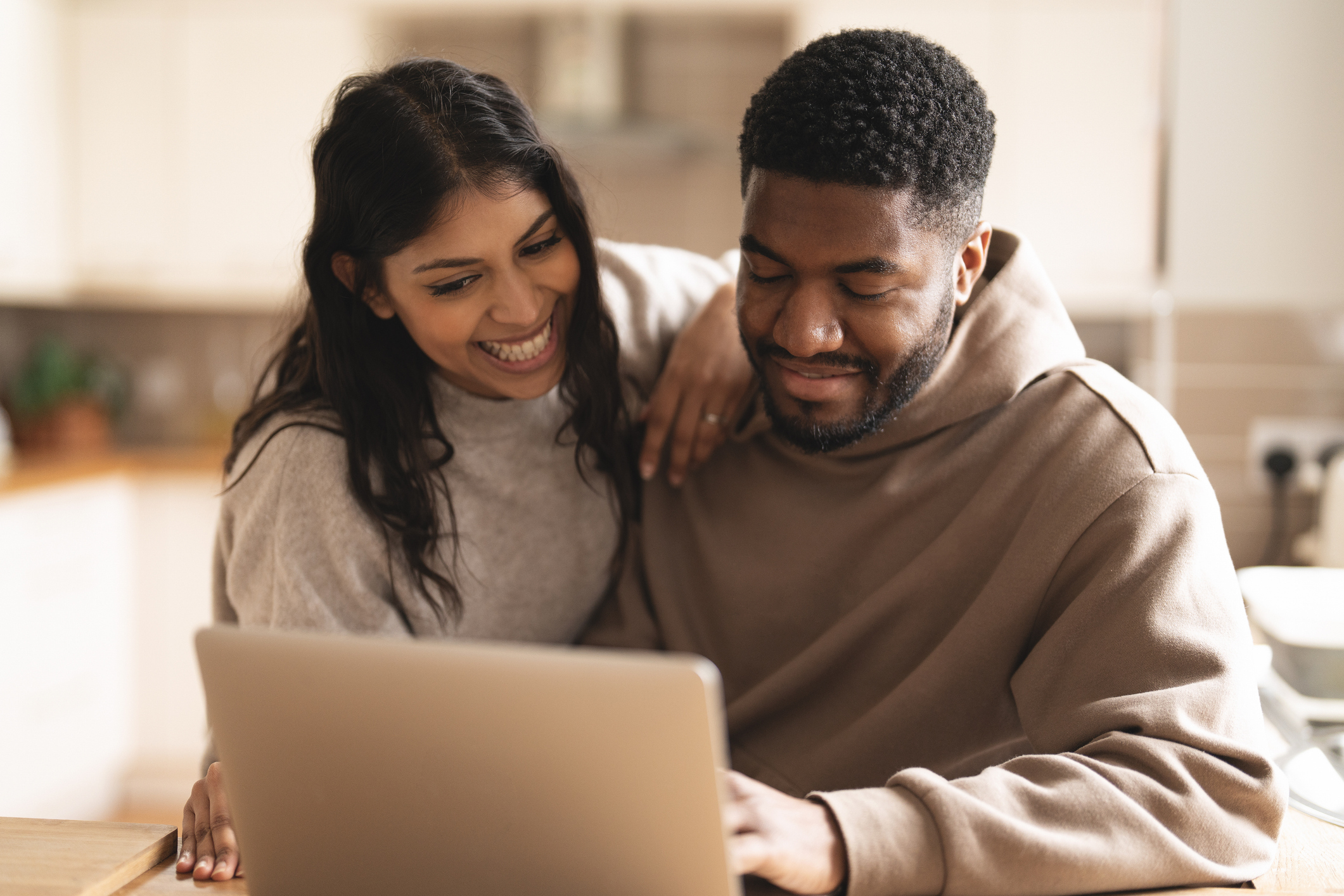 A man and a woman smiling while looking at a laptop.