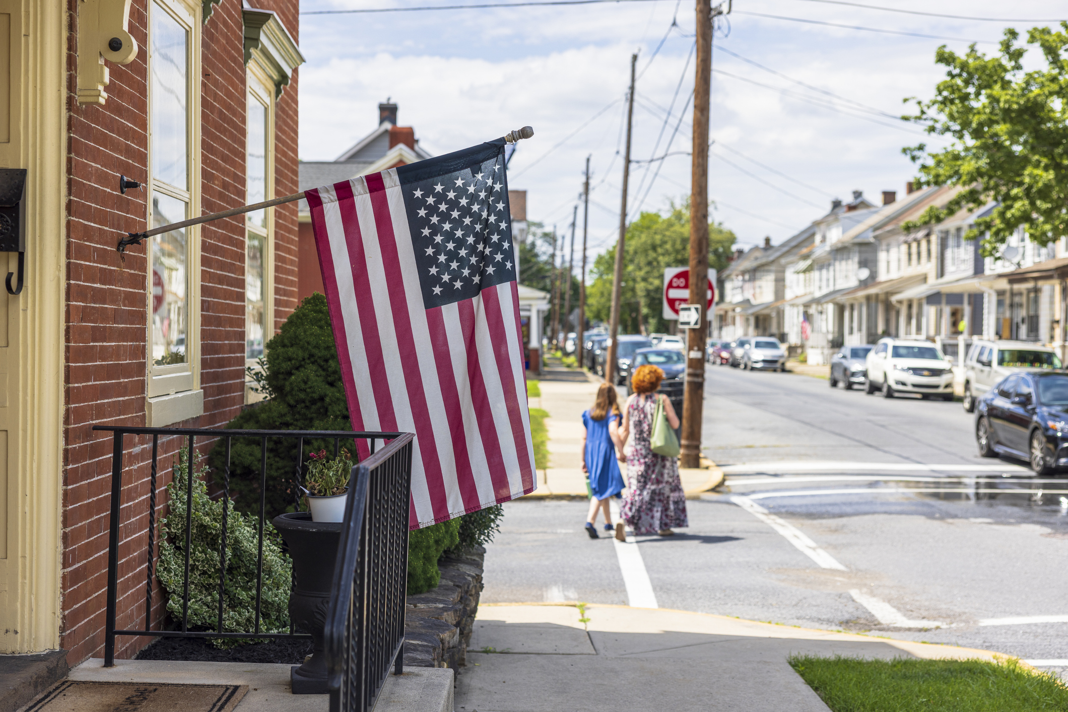 People walk in a small town with the American flag in the foreground.