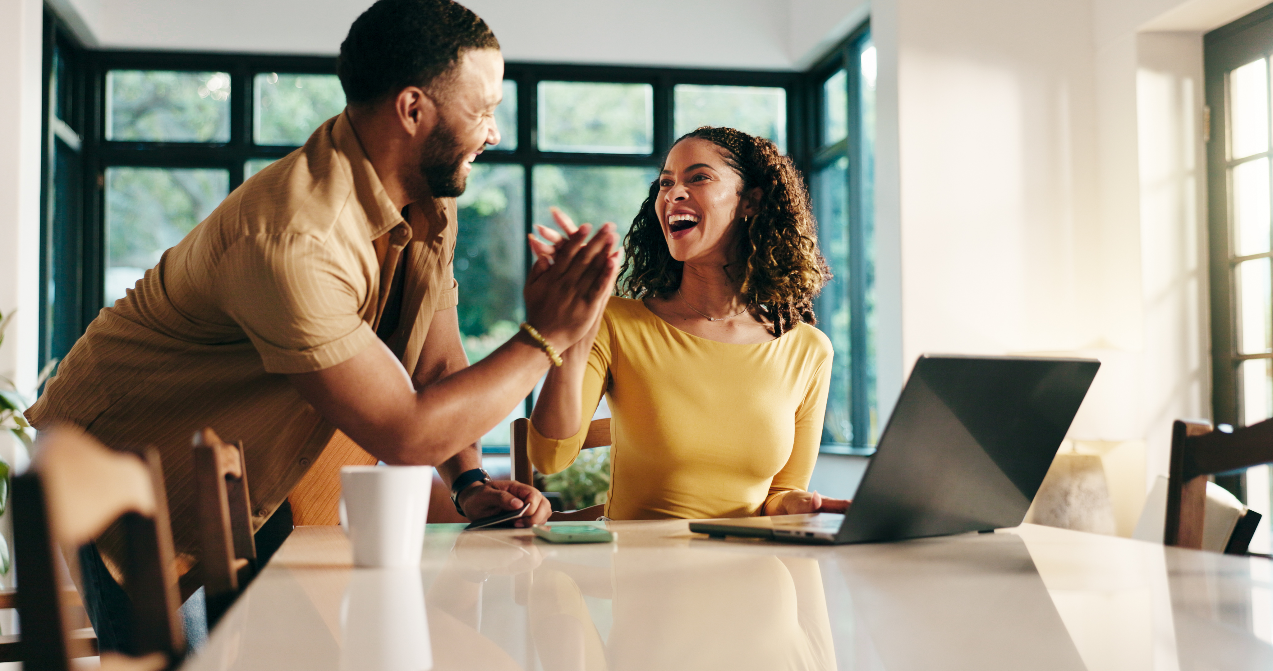 A couple high hives at a kitchen table in front of an open laptop.