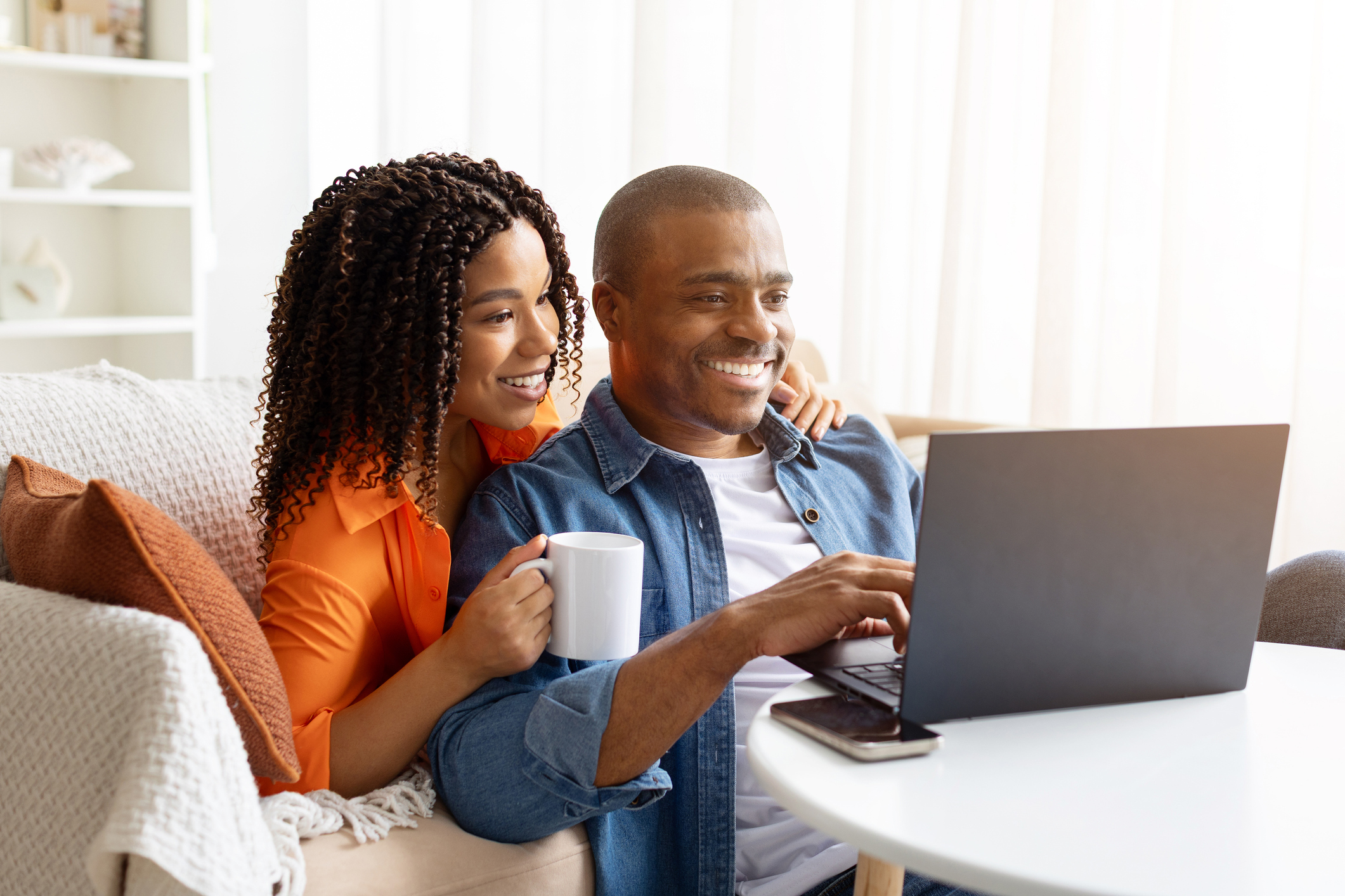 A man and a woman smile while drinking coffee and looking at a laptop.