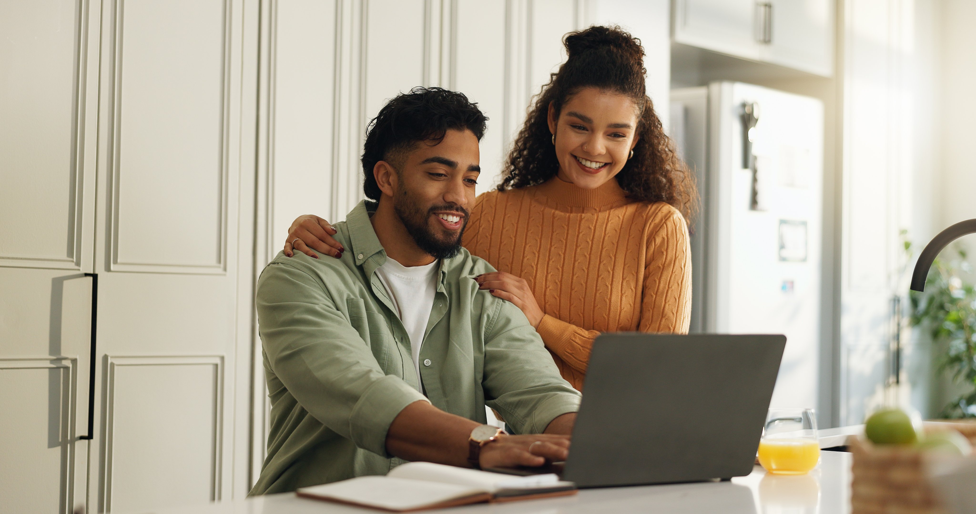 A man and a woman smiling while using a laptop.