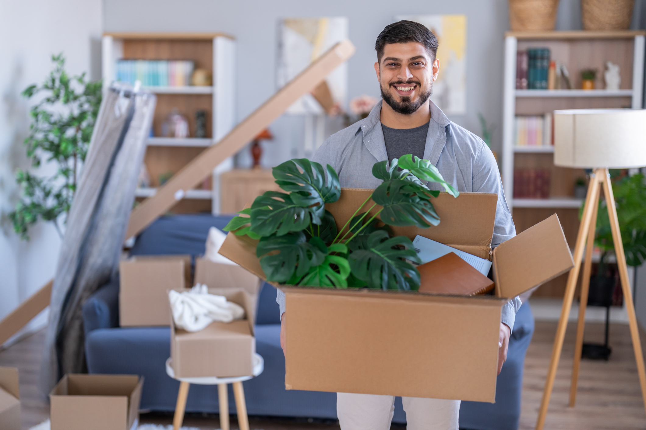 A man smiles while carrying moving boxes into a house.
