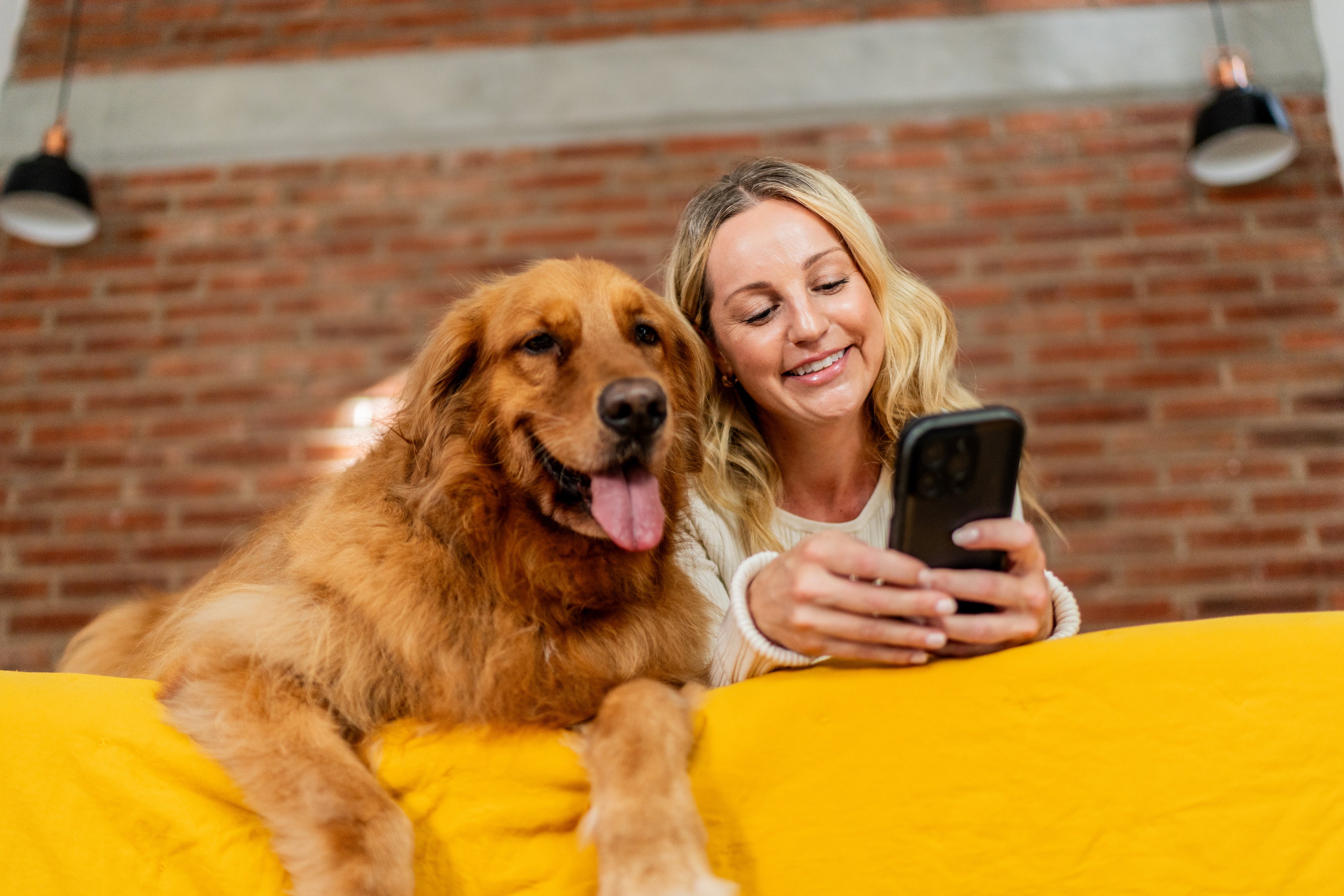 A woman and golden retriever smile at a phone.