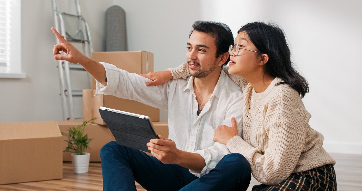 A man and a woman smile while moving into a house.