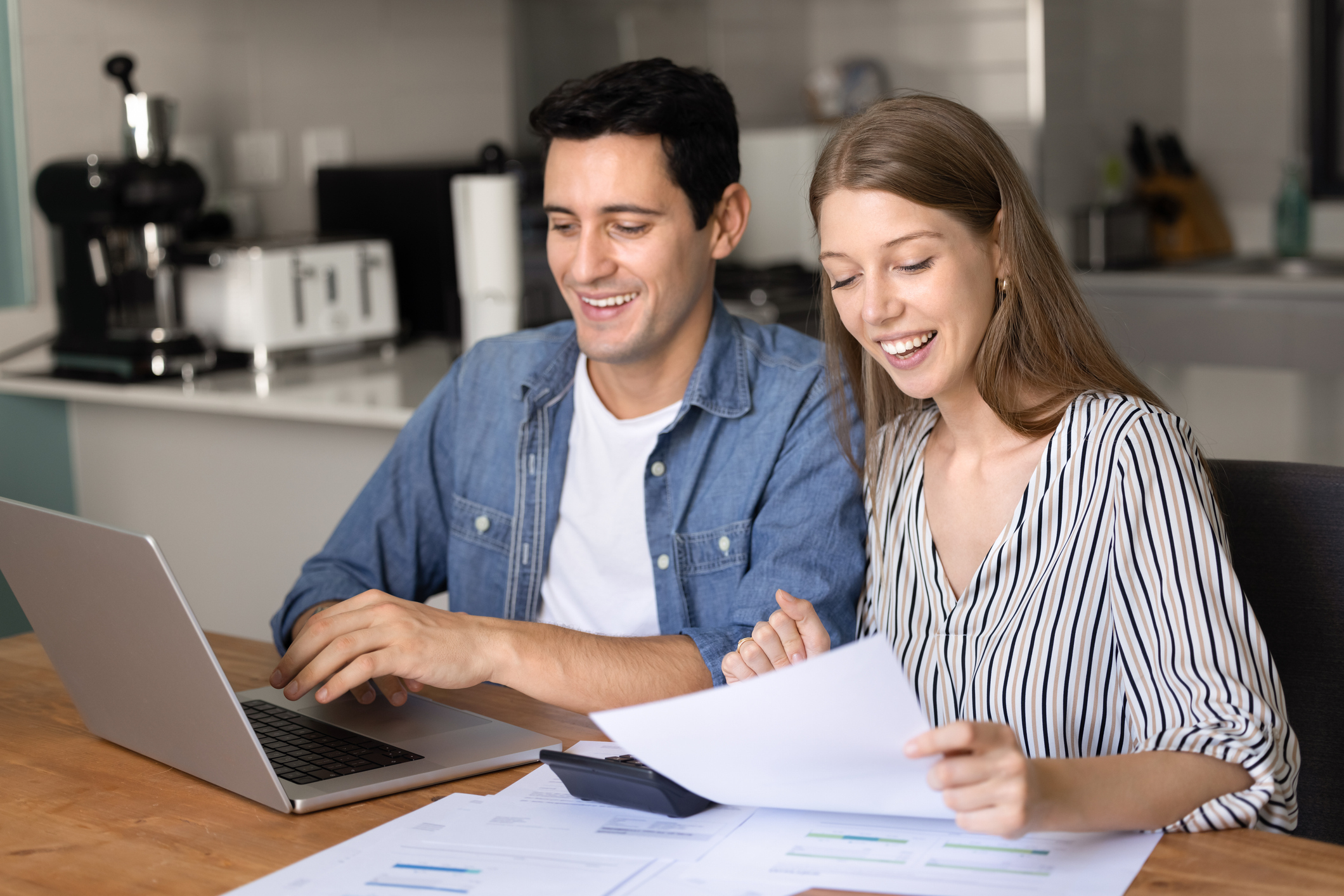 A man and a woman smiling at a laptop and papers. 