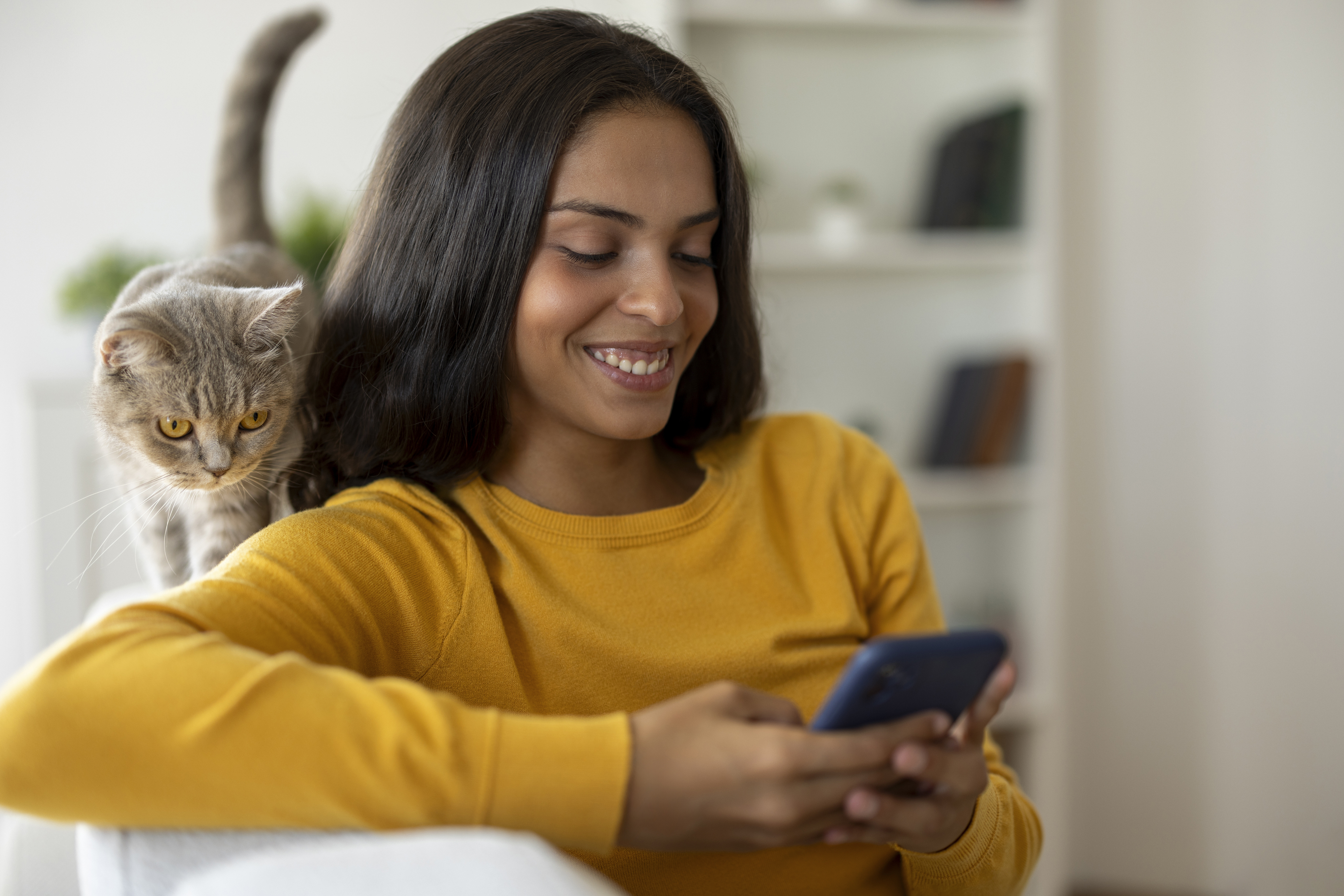 A woman smiles at a phone while hanging out with a cat.