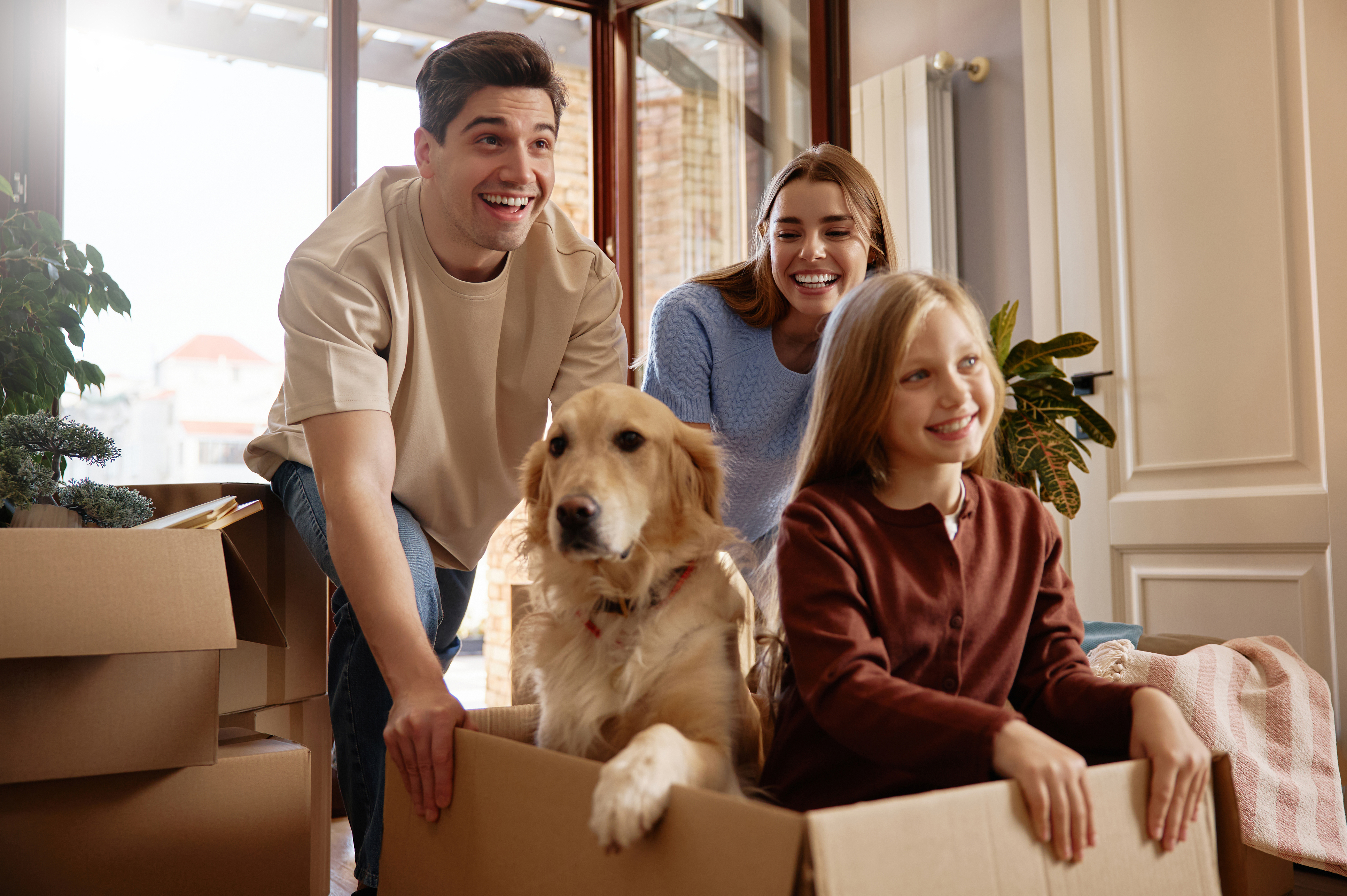 A family with a golden retriever smiling while moving into a house. 