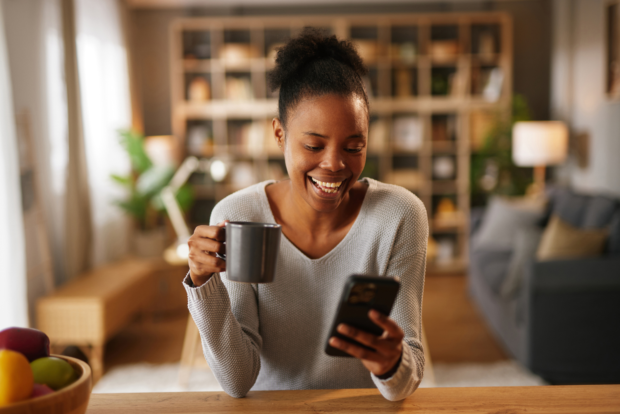 A woman smiles at a phone while sipping coffee.