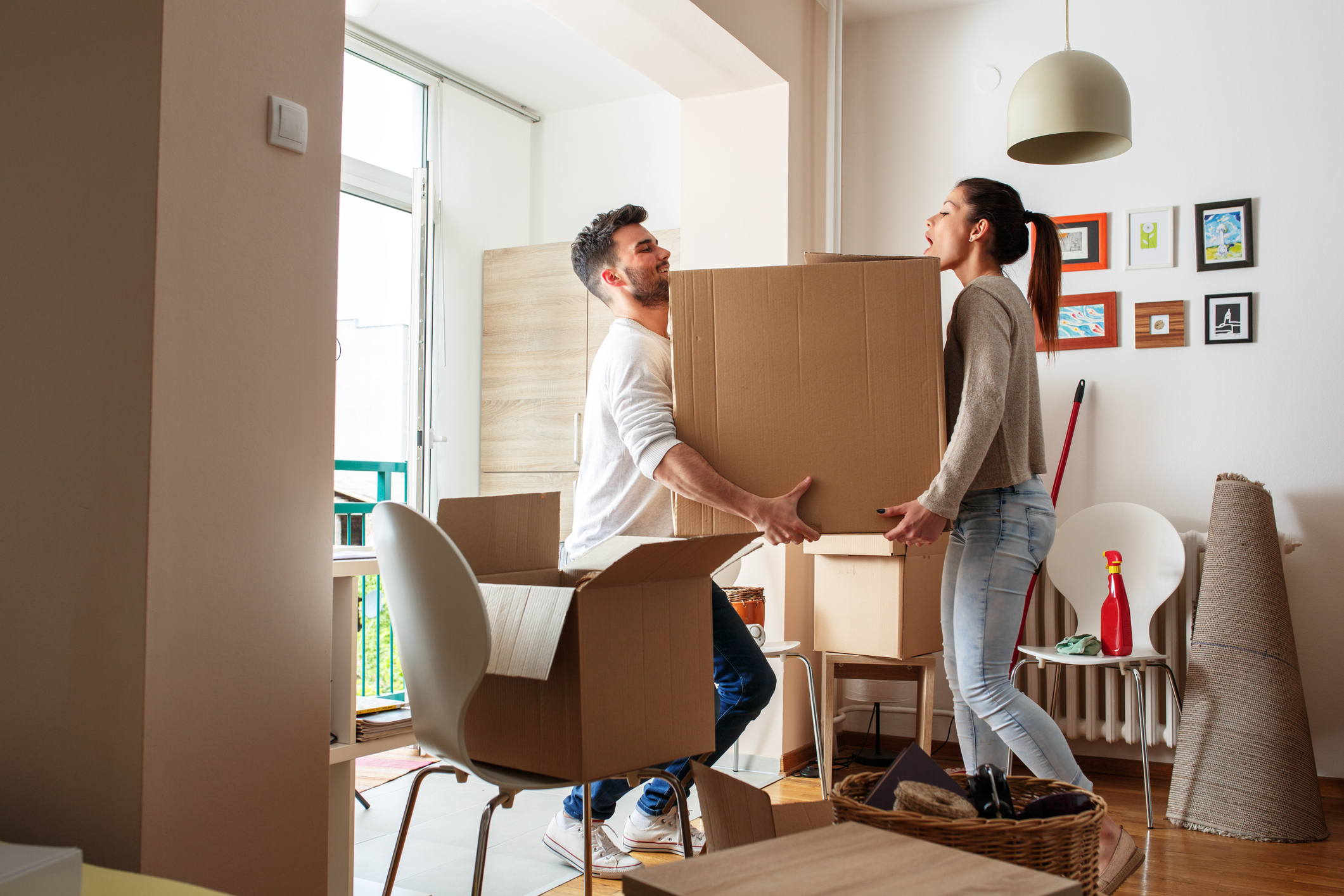 A man and a woman laugh while they carry a large box into a house.