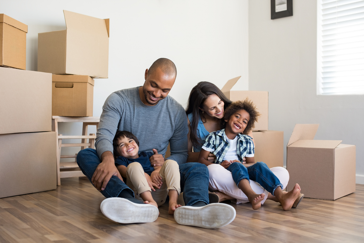 A man, woman and two young children smile while surrounded by boxes for moving.