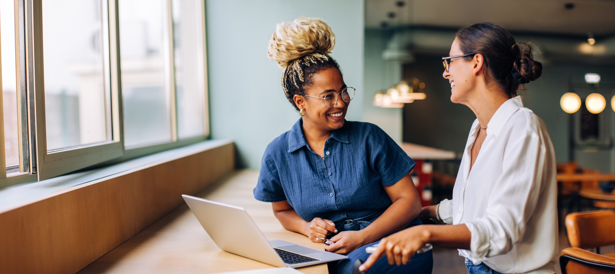 Two women smile while looking at a laptop.