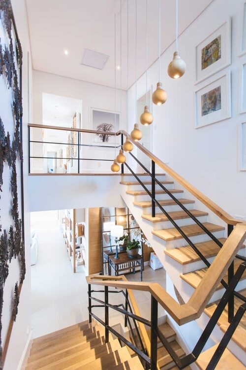 A wooden staircase in a modern home with white walls and hanging lights. 