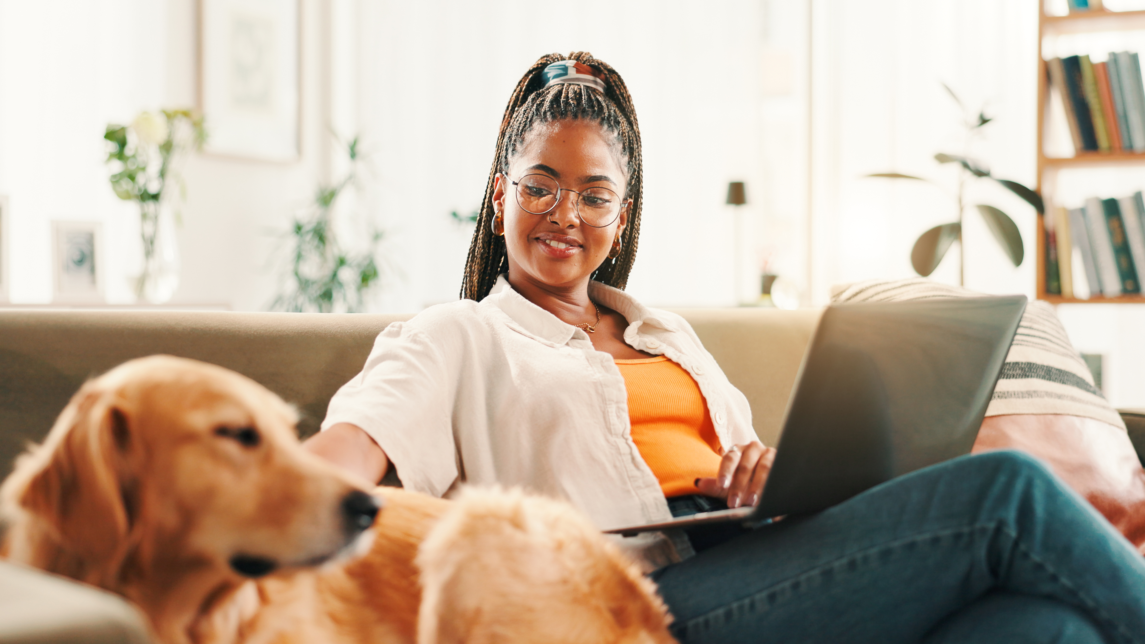 A woman smiles while working on a laptop next to her golden retriever. 